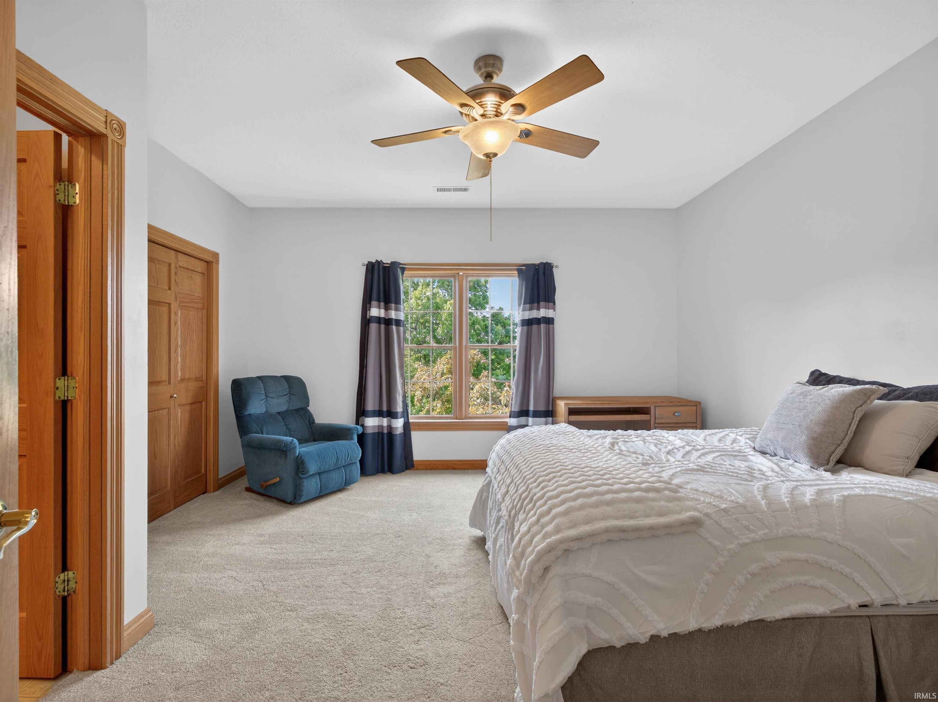 Carpeted room featuring a ceiling fan with integrated lighting, wood-trimmed window, and bi-fold closet doors