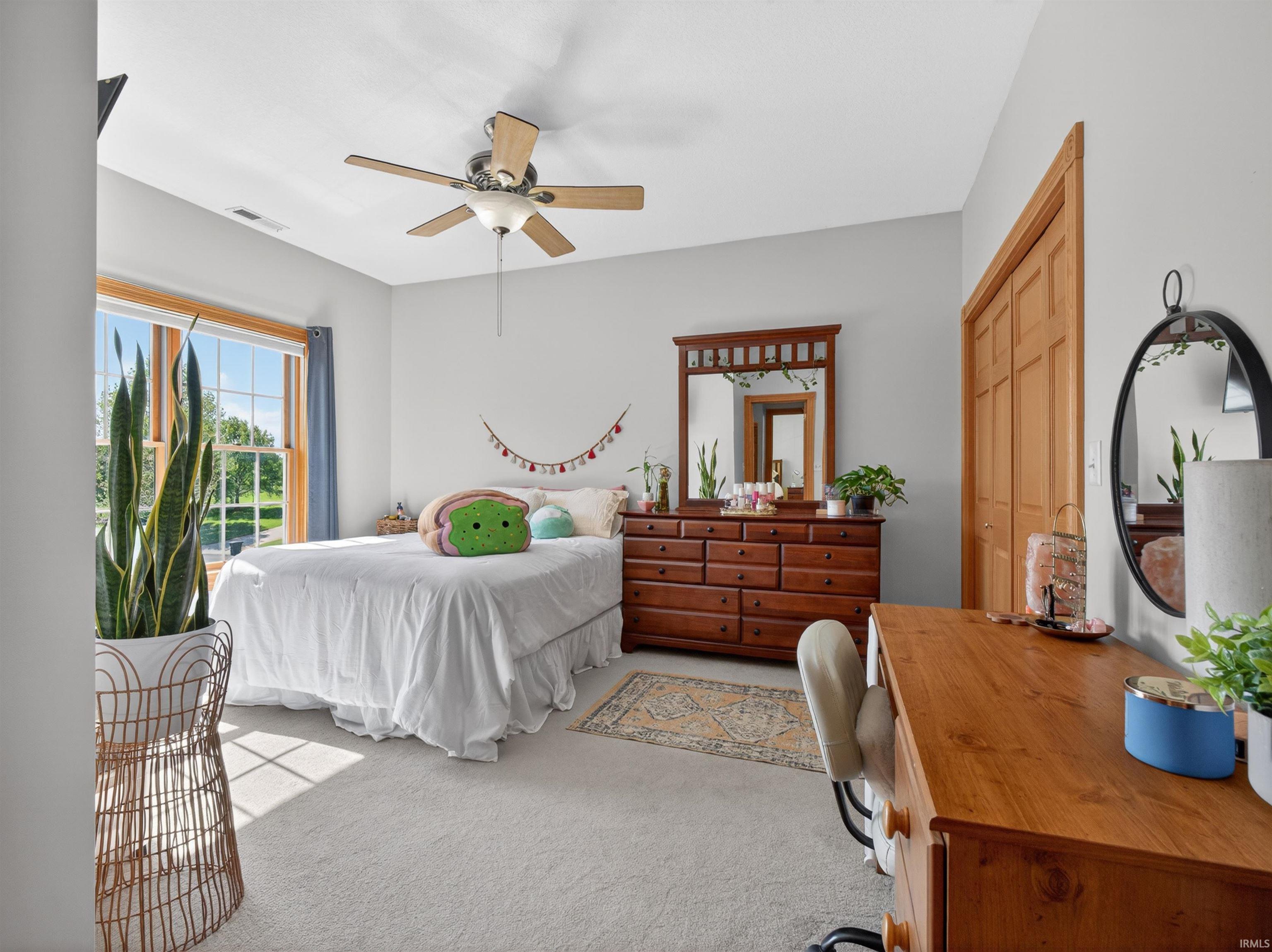 Carpeted room featuring a ceiling fan with light fixture, large window with wood trim, and a built-in closet with wood bifold doors