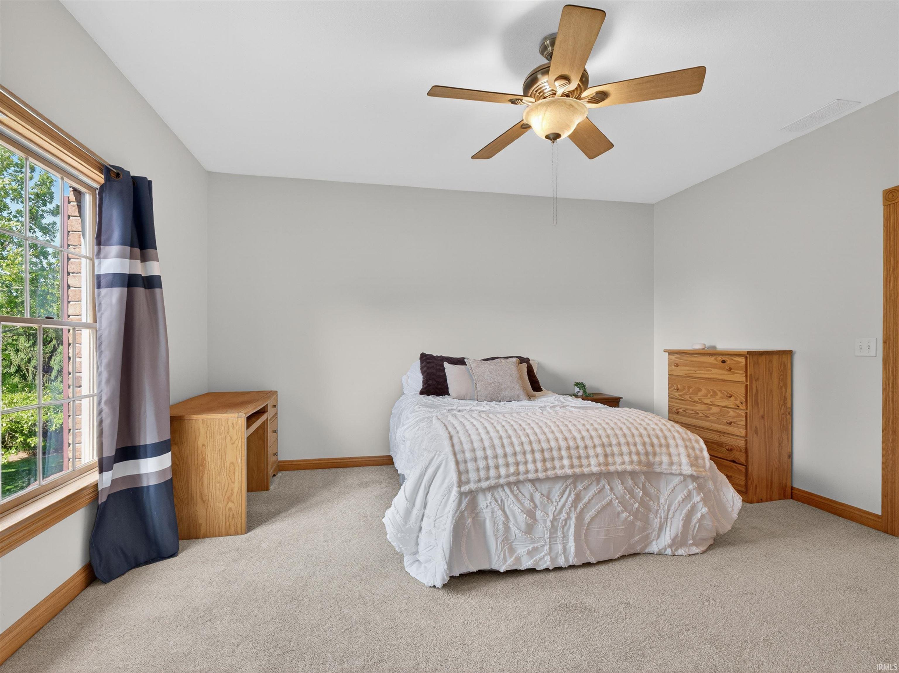 Carpeted room featuring a ceiling fan with light fixture, light-toned walls, and wood trim around the window and doorway