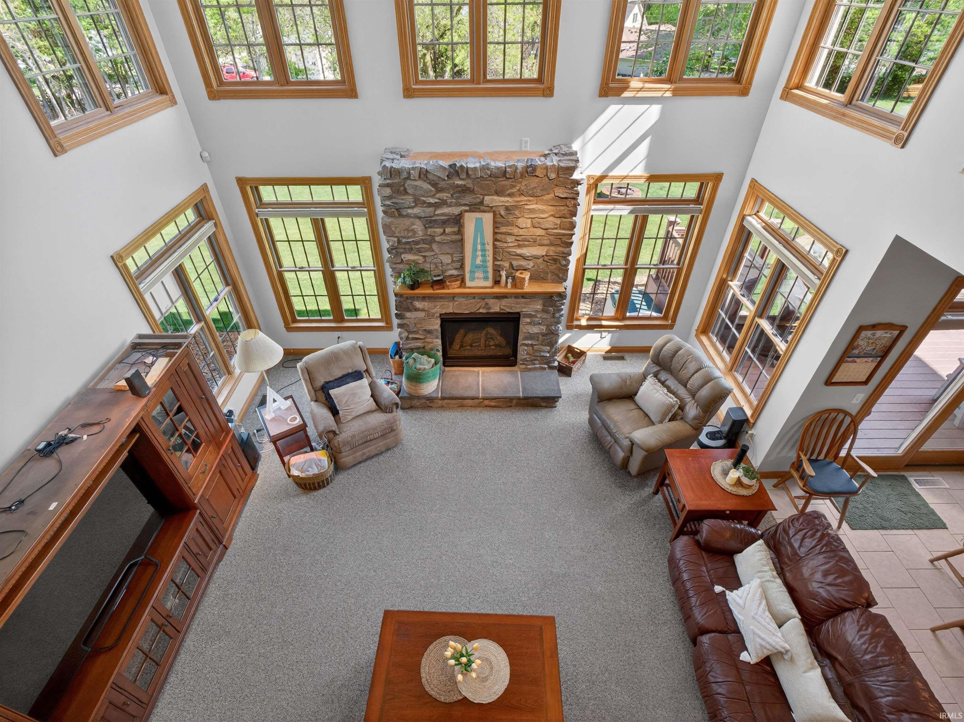 Great room featuring a floor-to-ceiling stone fireplace, vaulted ceilings, and numerous wood-framed windows