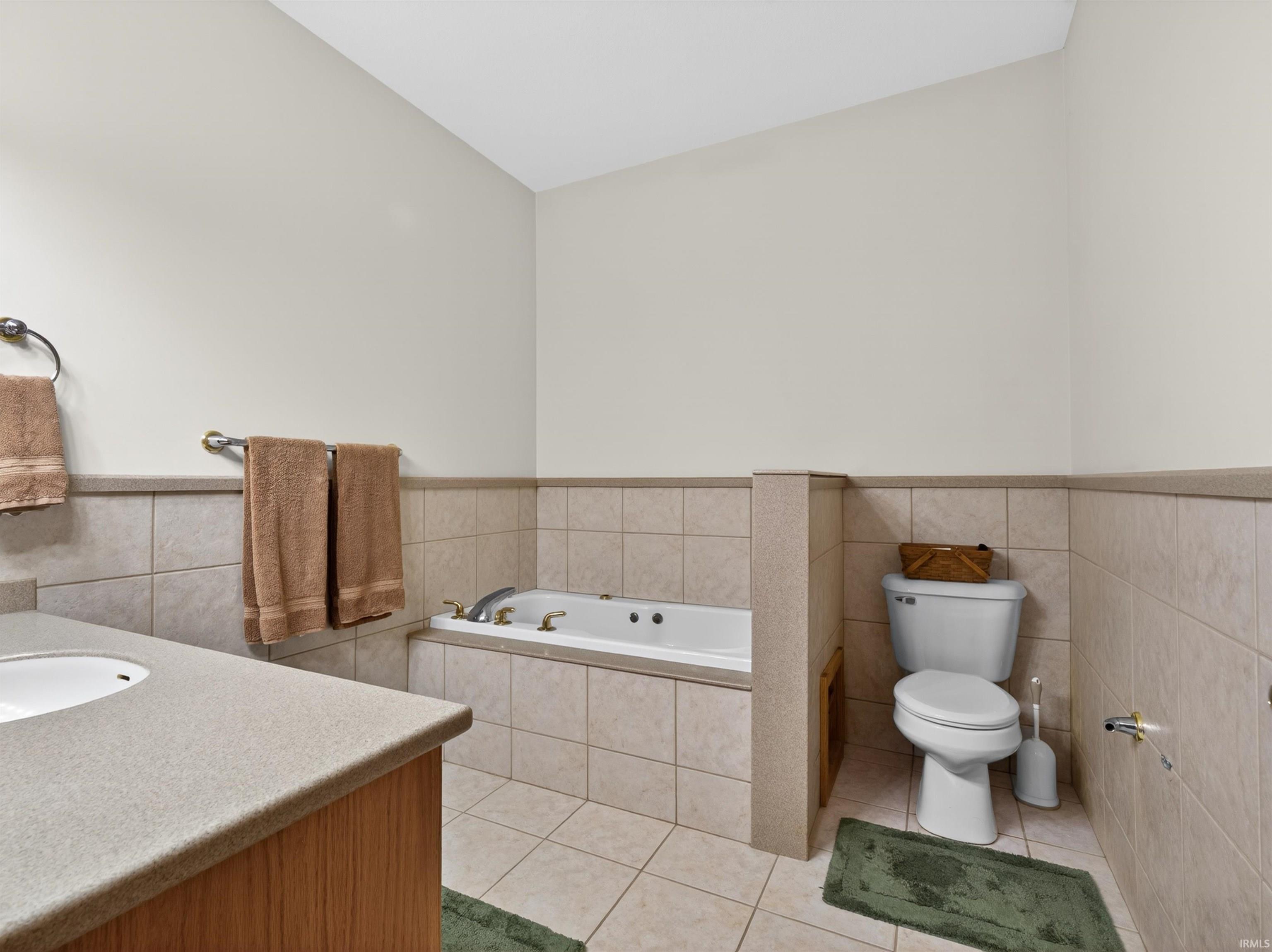 Bathroom featuring a built-in jetted tub, ceramic tile flooring, and a tiled half-wall surround