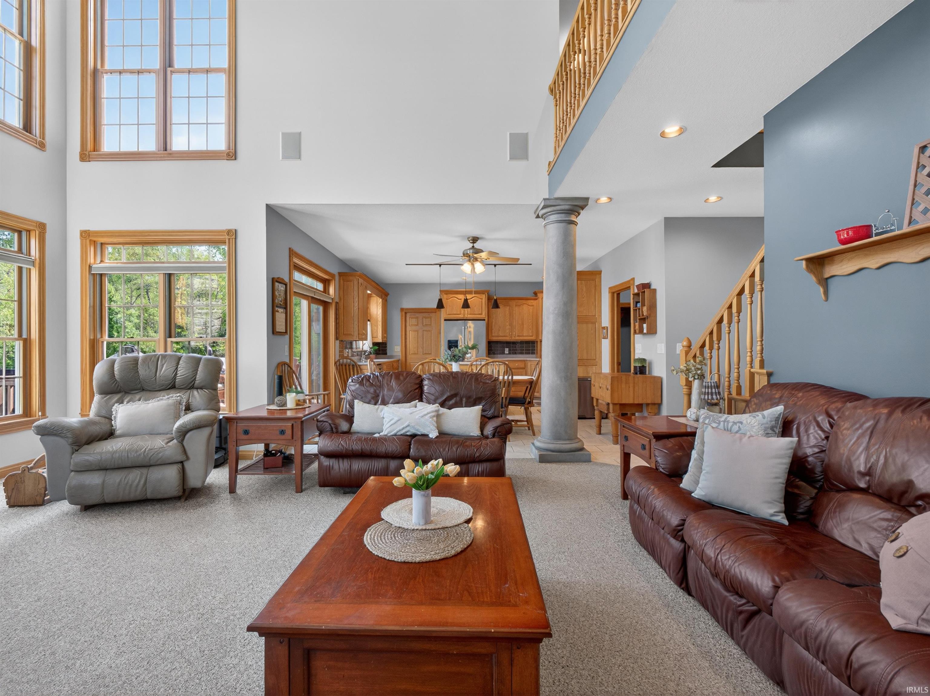 Spacious living area featuring a two-story ceiling, large picture windows, light-toned carpet flooring, and a decorative column