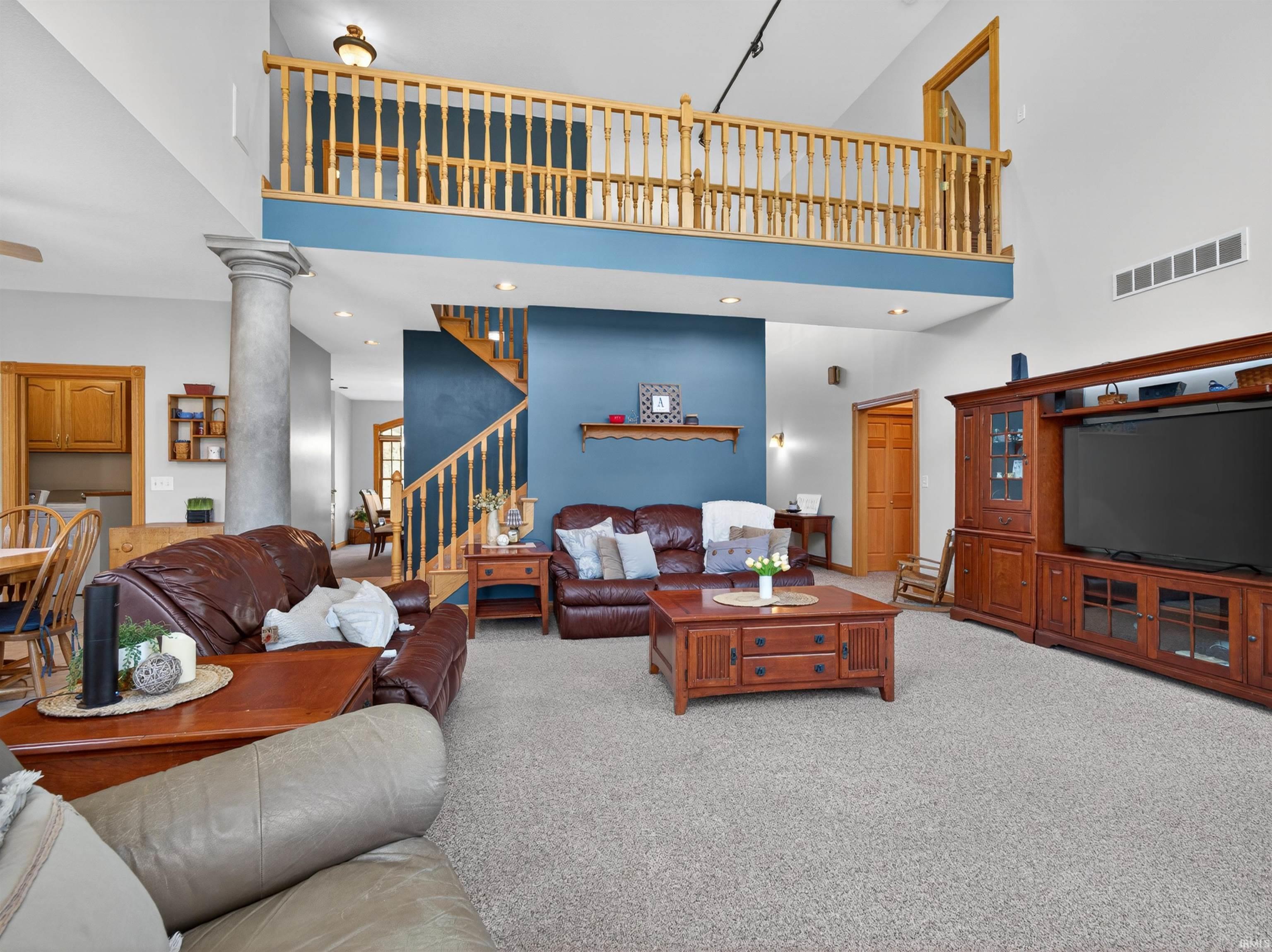 Spacious living area featuring a two-story ceiling, architectural column, and an upper-level balcony with a wood railing