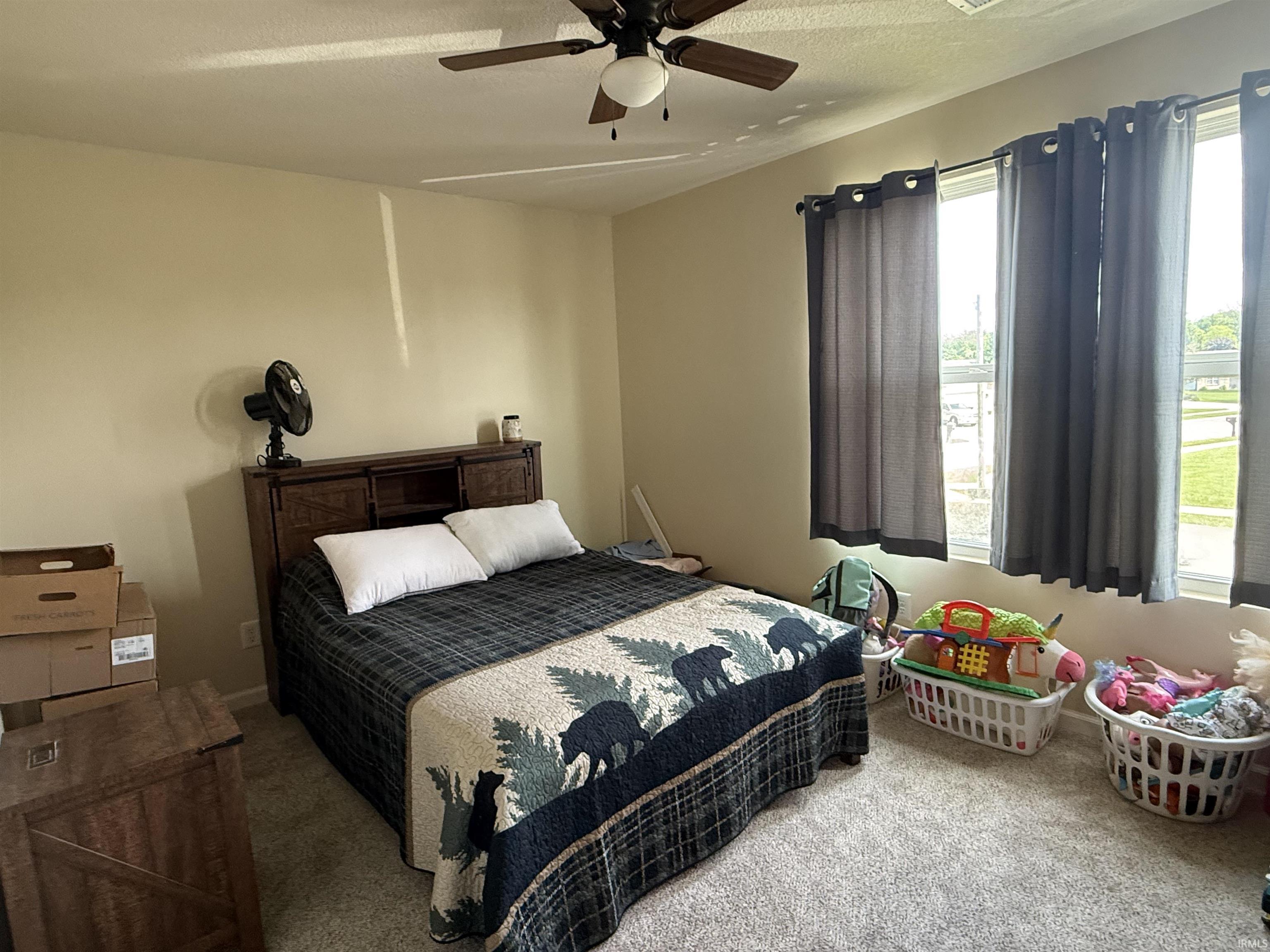 Carpeted bedroom featuring a ceiling fan with integrated lighting, multiple windows providing natural light, and neutral wall tones