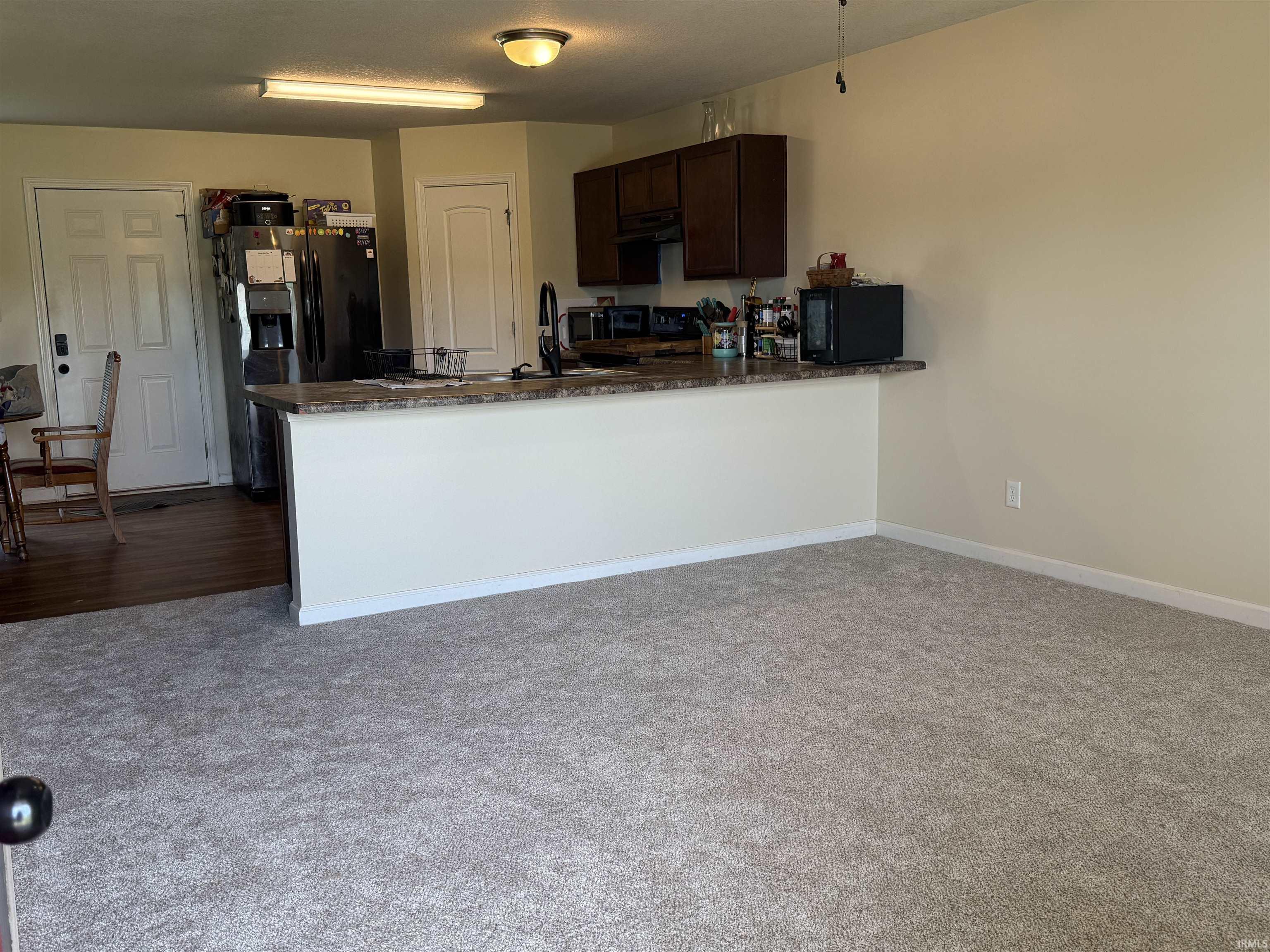 Open-concept living space featuring a carpeted area and a kitchen with wood-finish flooring