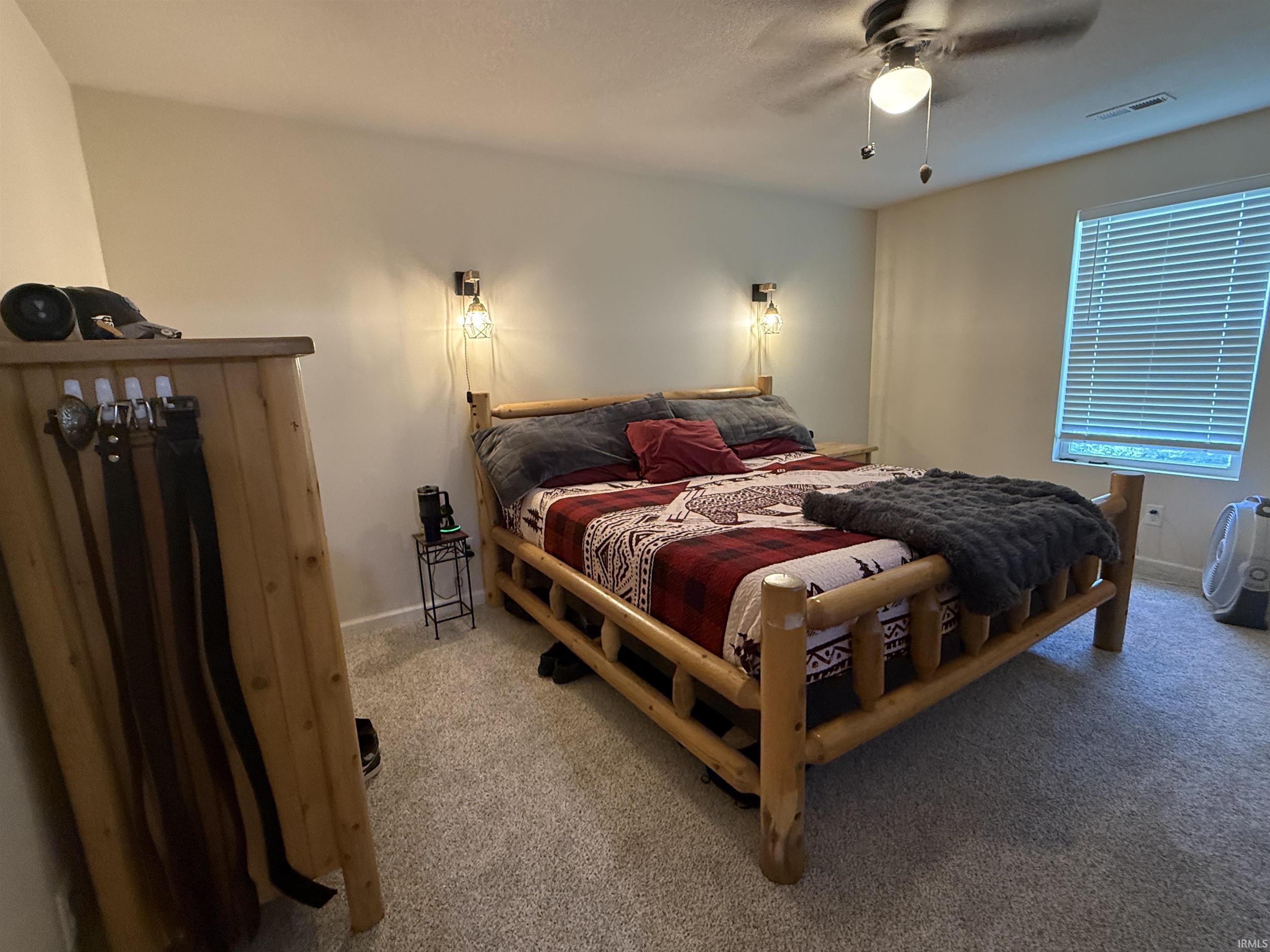 Carpeted room featuring a ceiling fan with integrated lighting, a window with horizontal blinds, and wall-mounted sconce lighting