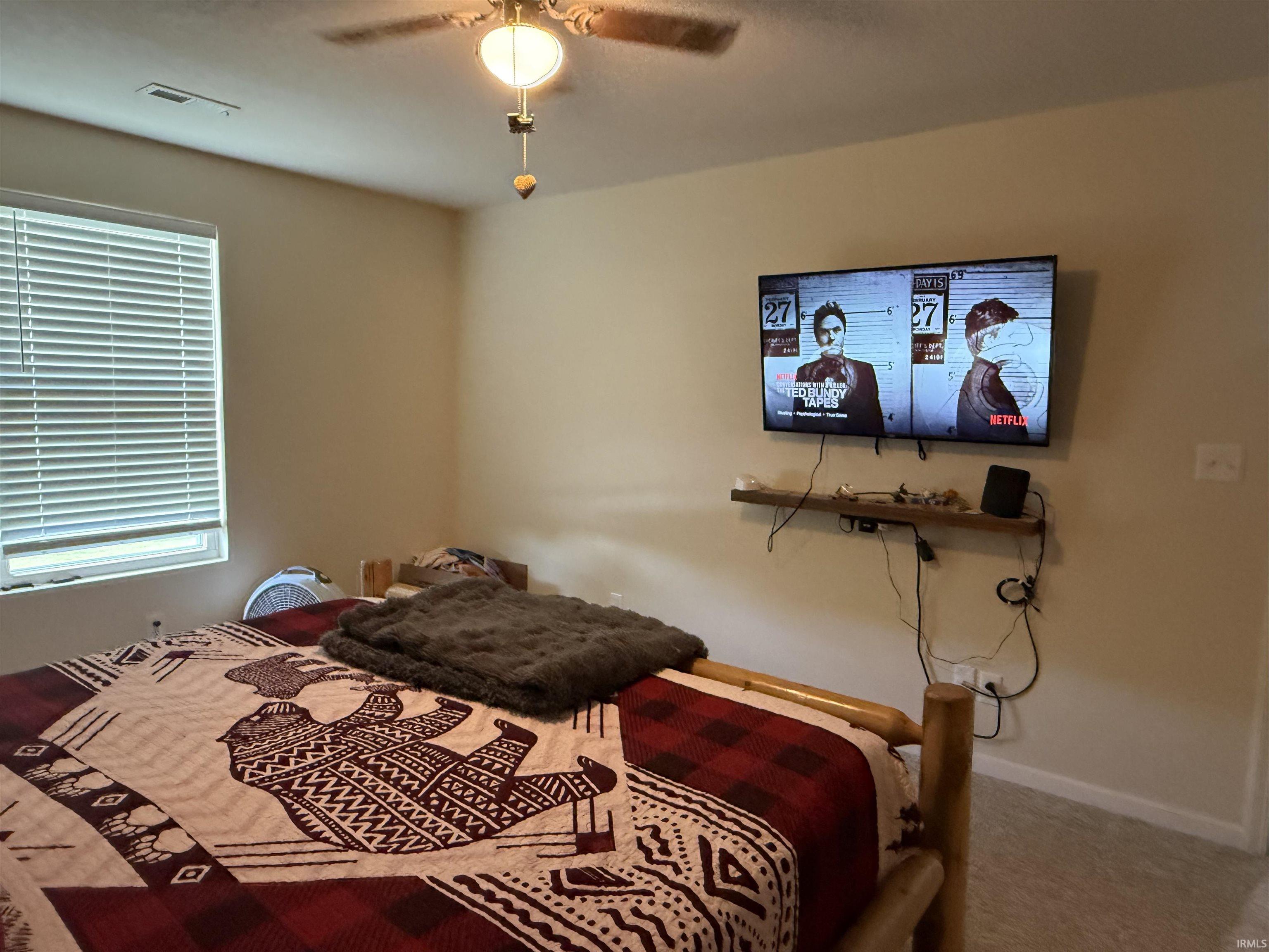 Bedroom featuring a ceiling fan with integrated lighting, a window with horizontal blinds, neutral-toned walls, and grey carpeting