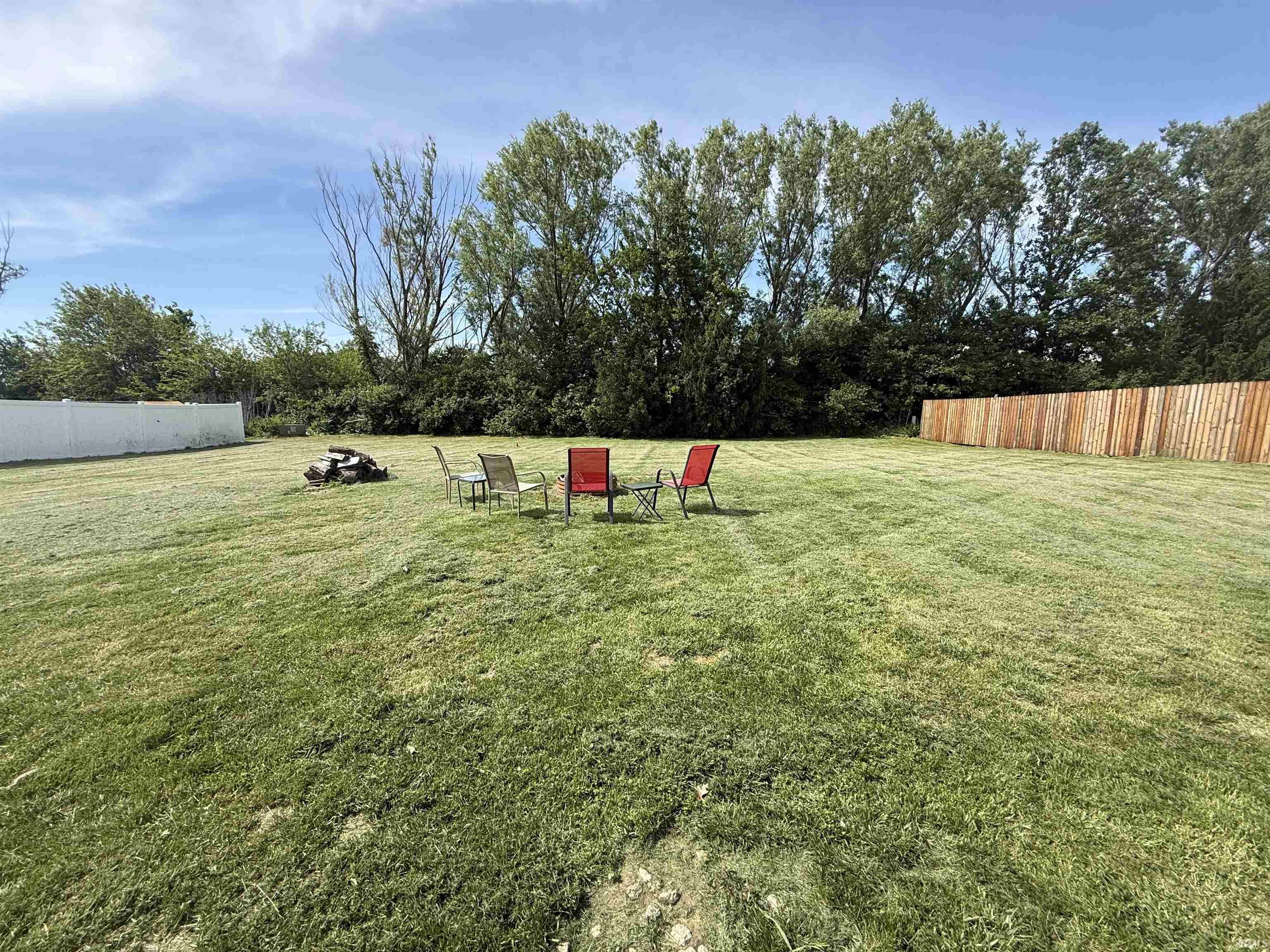 Expansive backyard featuring a manicured lawn, a white privacy fence, a wood privacy fence, and mature trees along the perimeter