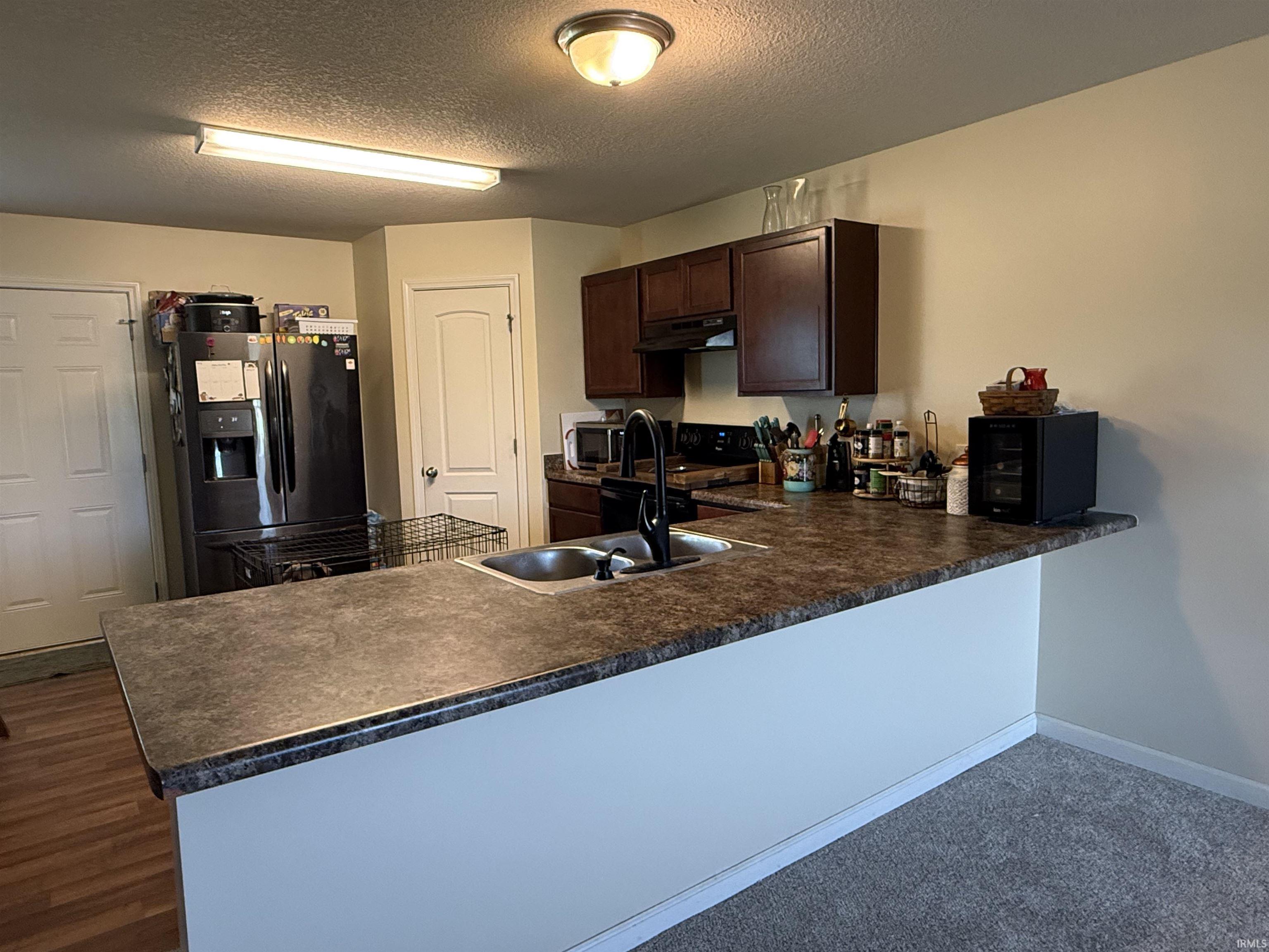 Kitchen featuring an expansive breakfast bar with a stone-finish countertop, a double basin stainless steel sink, and dark wood cabinetry