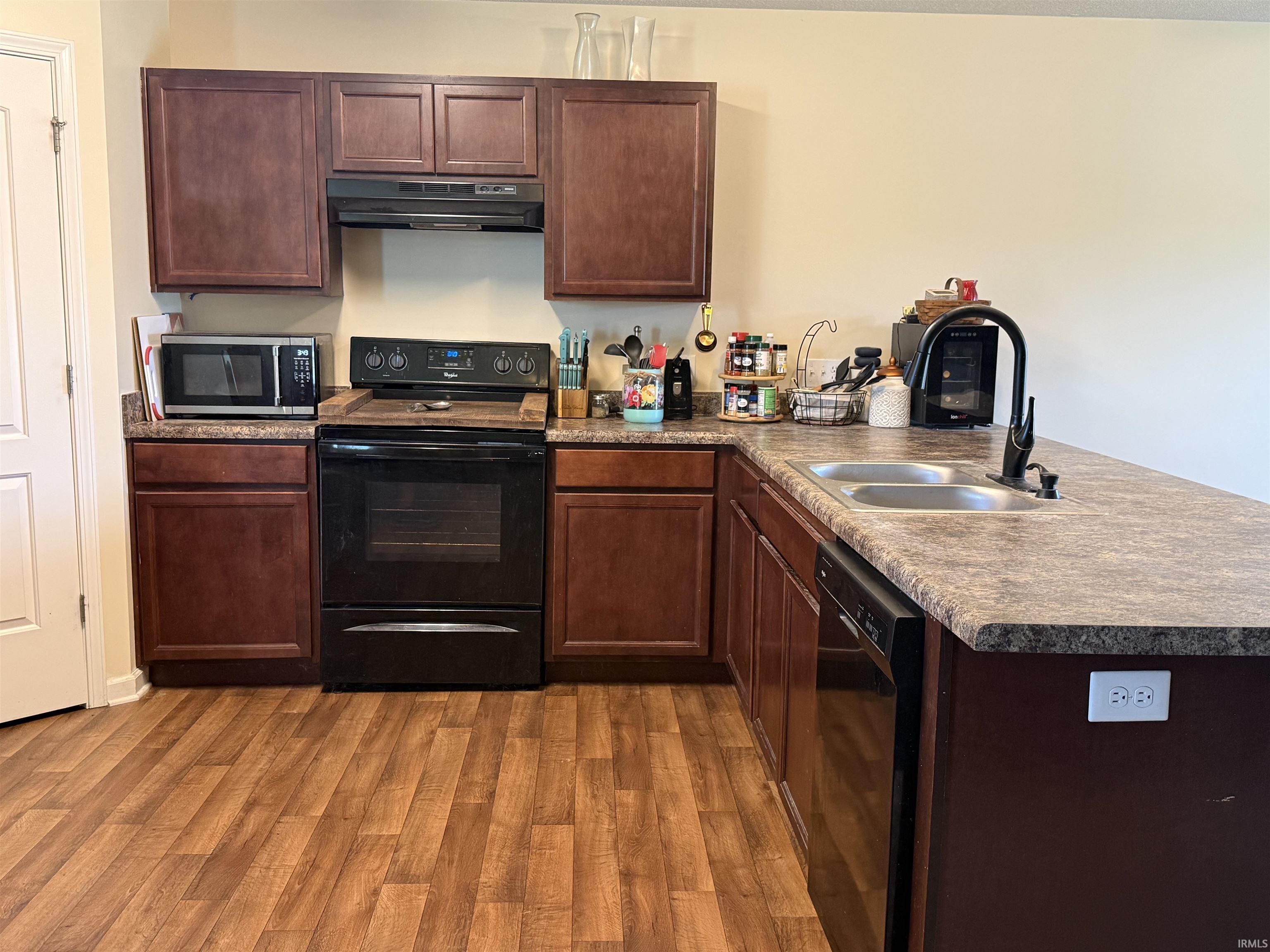 Kitchen featuring dark wood-finish cabinetry, wood-finish flooring, a double basin sink with a black gooseneck faucet, black electric range, and a black built-in dishwasher