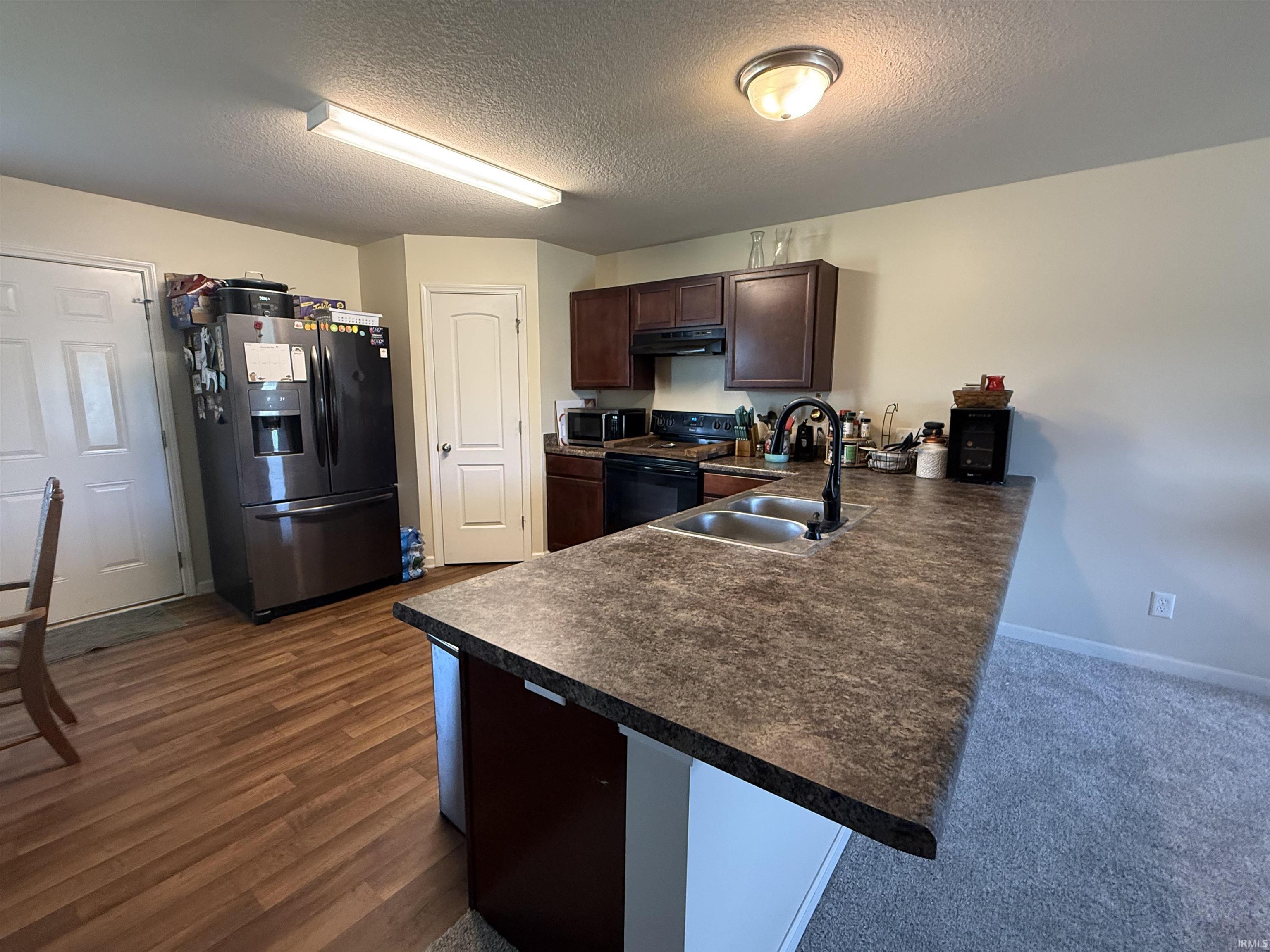 Kitchen featuring a double basin sink with a matte black faucet, wood-finish flooring, dark wood cabinetry, and a countertop island with seating space