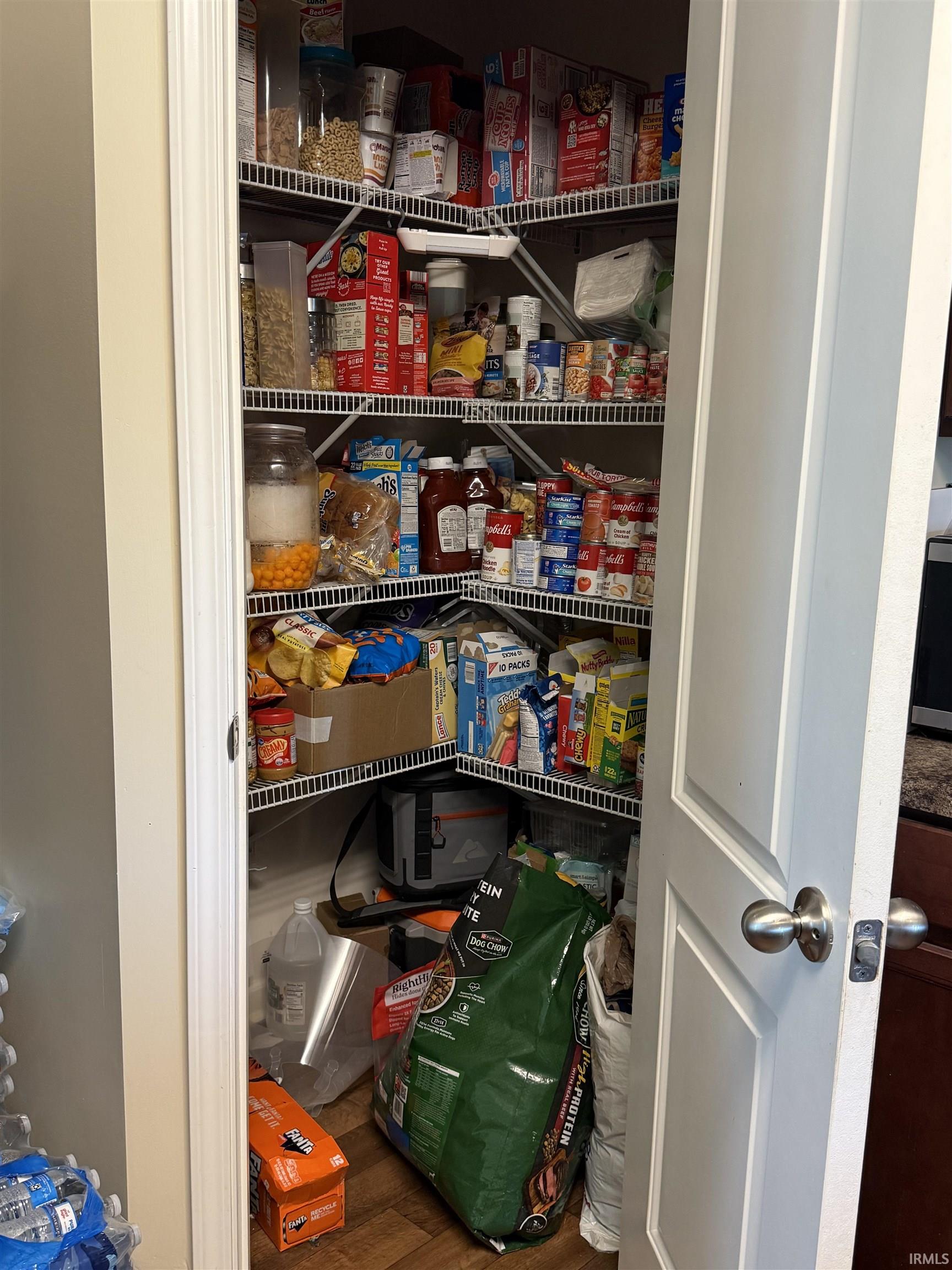 Corner pantry featuring multiple wire shelving units, a two-panel interior door with brushed nickel hardware, and wood-finish flooring