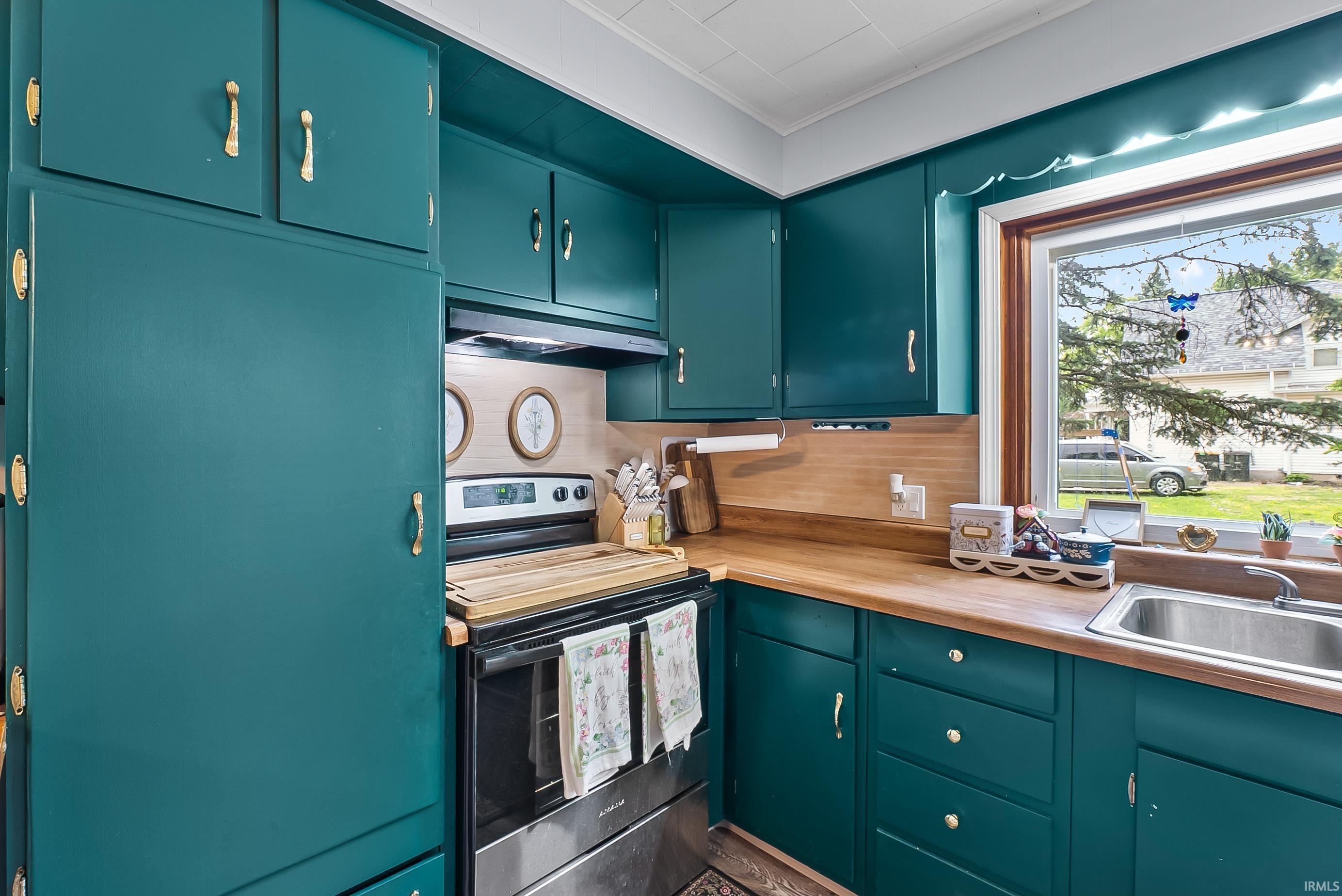 Kitchen featuring teal cabinetry with gold-tone hardware, wood-finish countertops, stainless steel sink, and a built-in range
