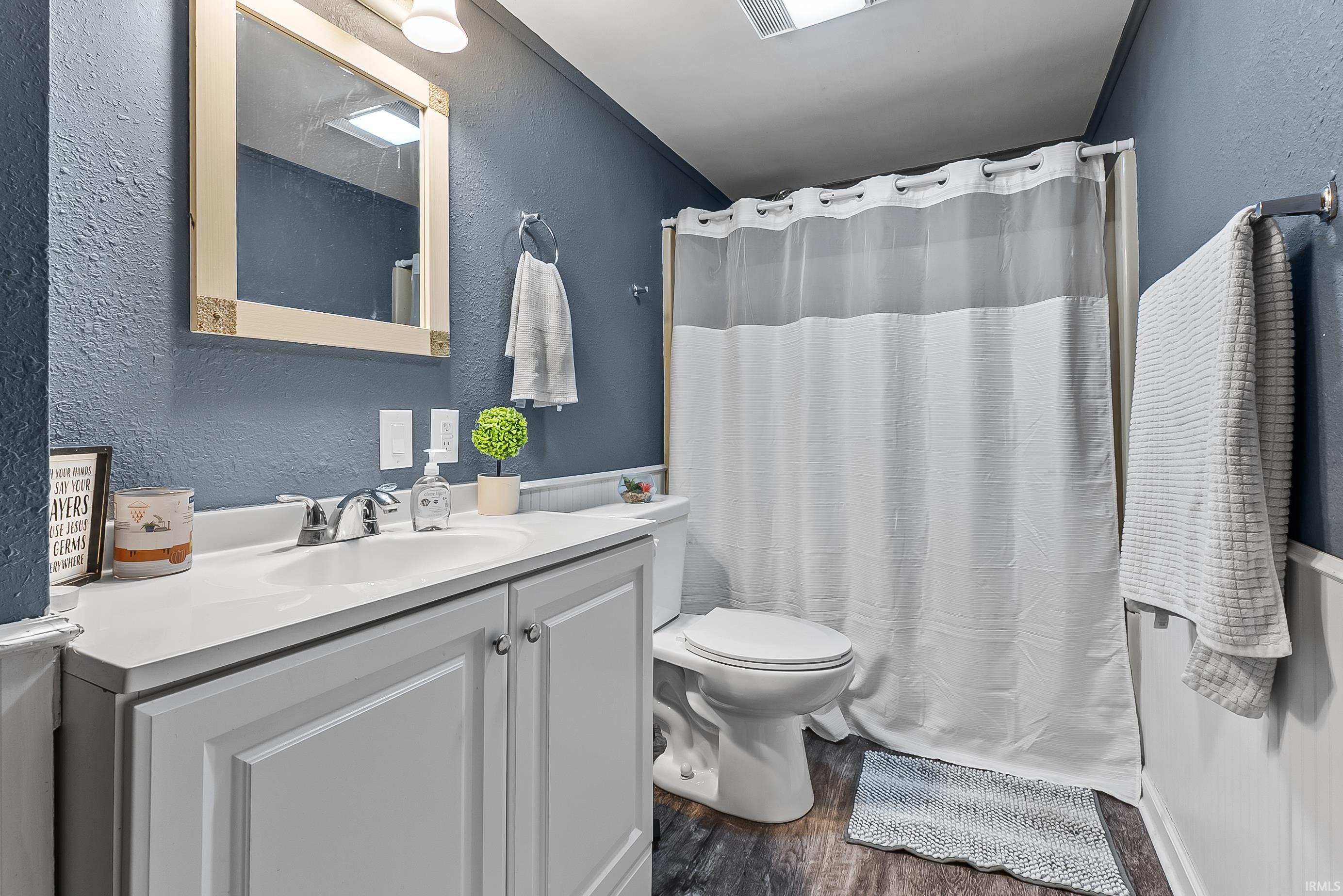Bathroom featuring a white vanity with integrated sink, chrome faucet, and wood-finish flooring