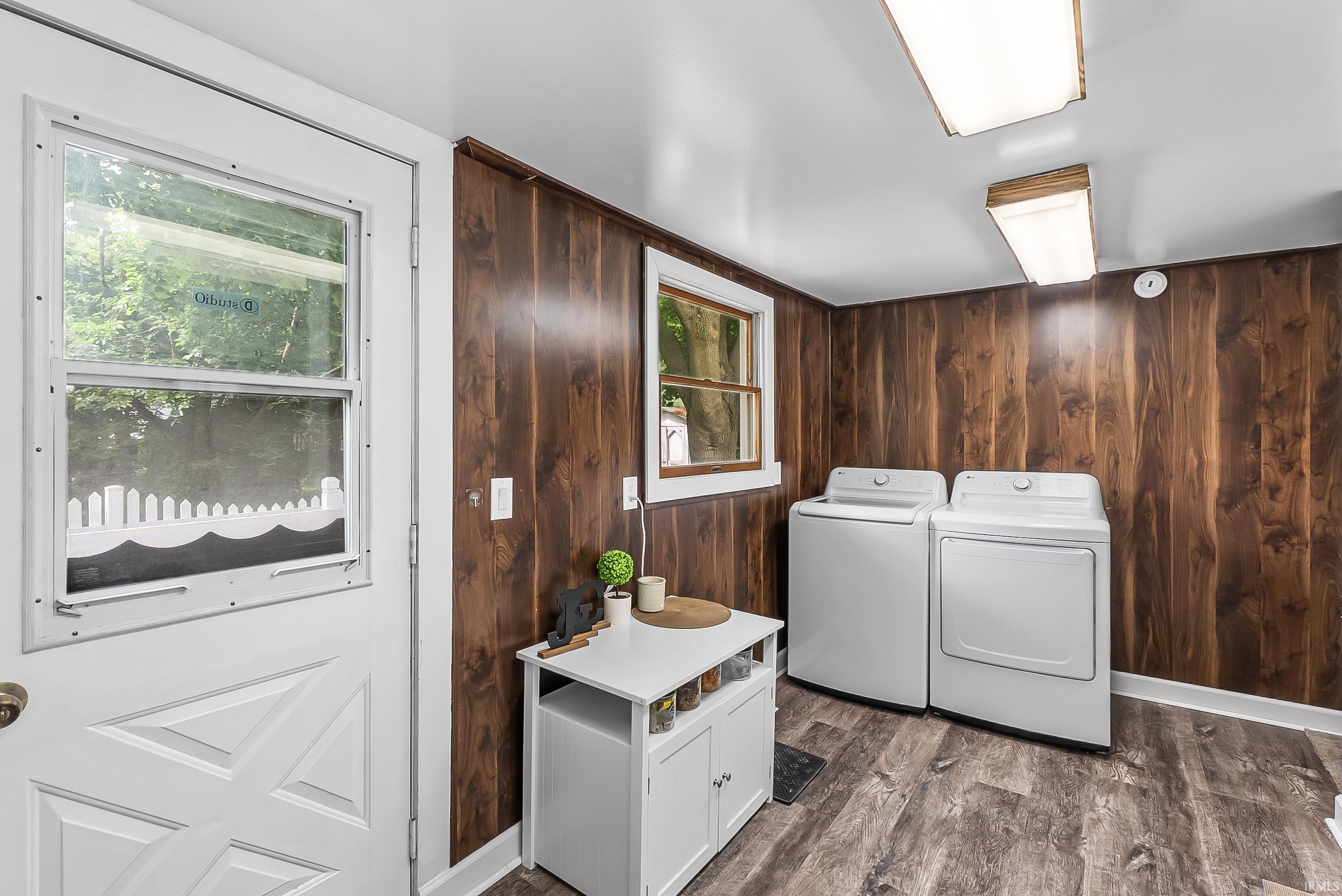 Dedicated laundry area featuring a white door with a window, wood-finish wall paneling, two fluorescent ceiling light fixtures, a window with wood trim, and wood-finish flooring