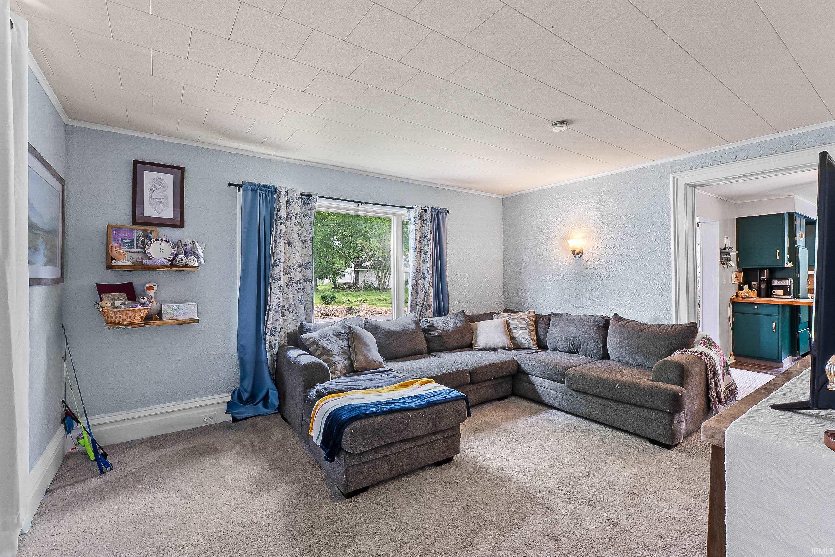 Carpeted living space featuring a window with exterior views, wall sconce lighting, and a neutral color palette