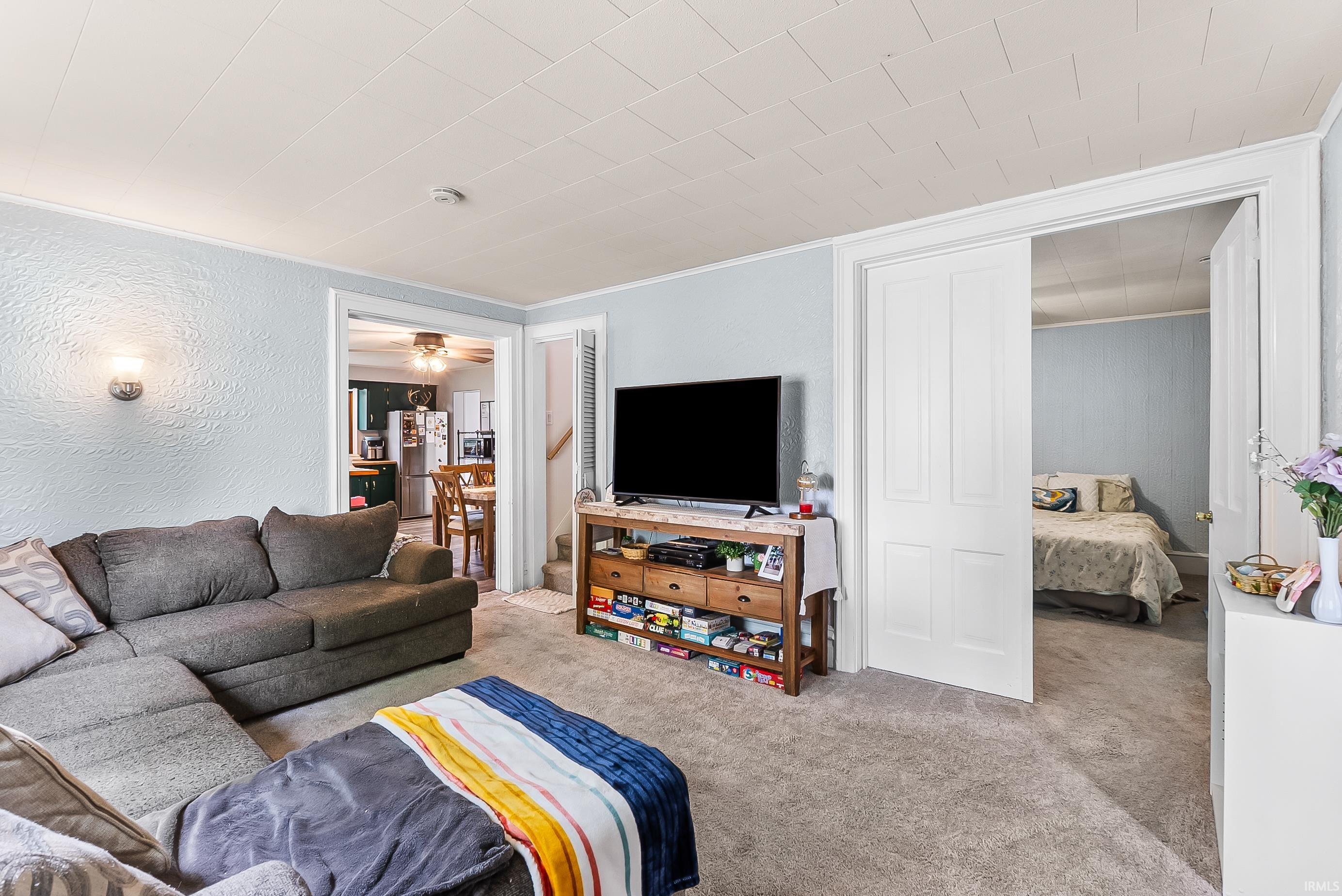 Living area featuring light blue textured walls, light gray carpet, and a white paneled ceiling