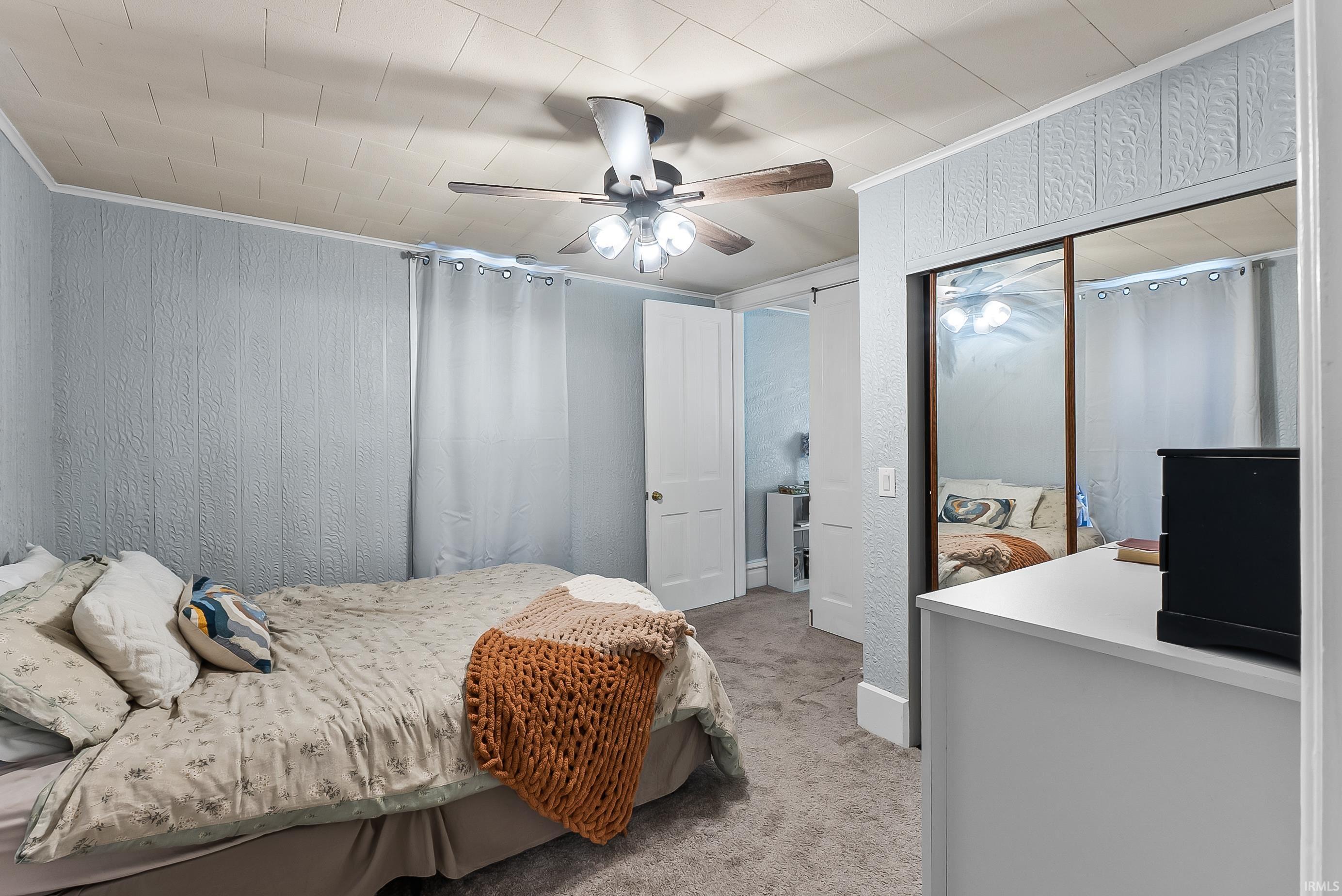 Carpeted bedroom with textured wall panels and a ceiling fan with light fixture