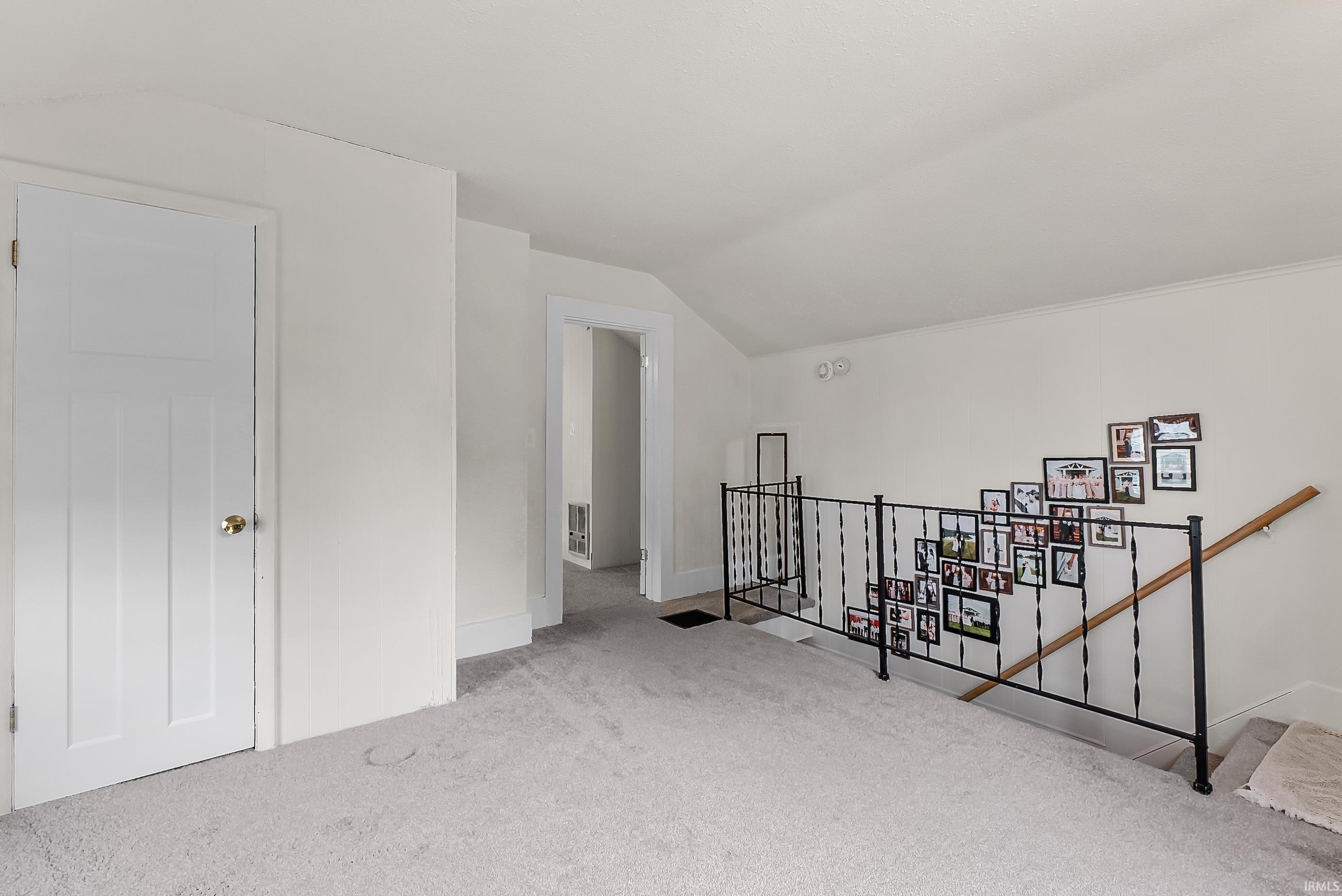 Spacious carpeted landing featuring a white paneled door, sculpted white baseboards, and a black wrought iron railing with wood handrail
