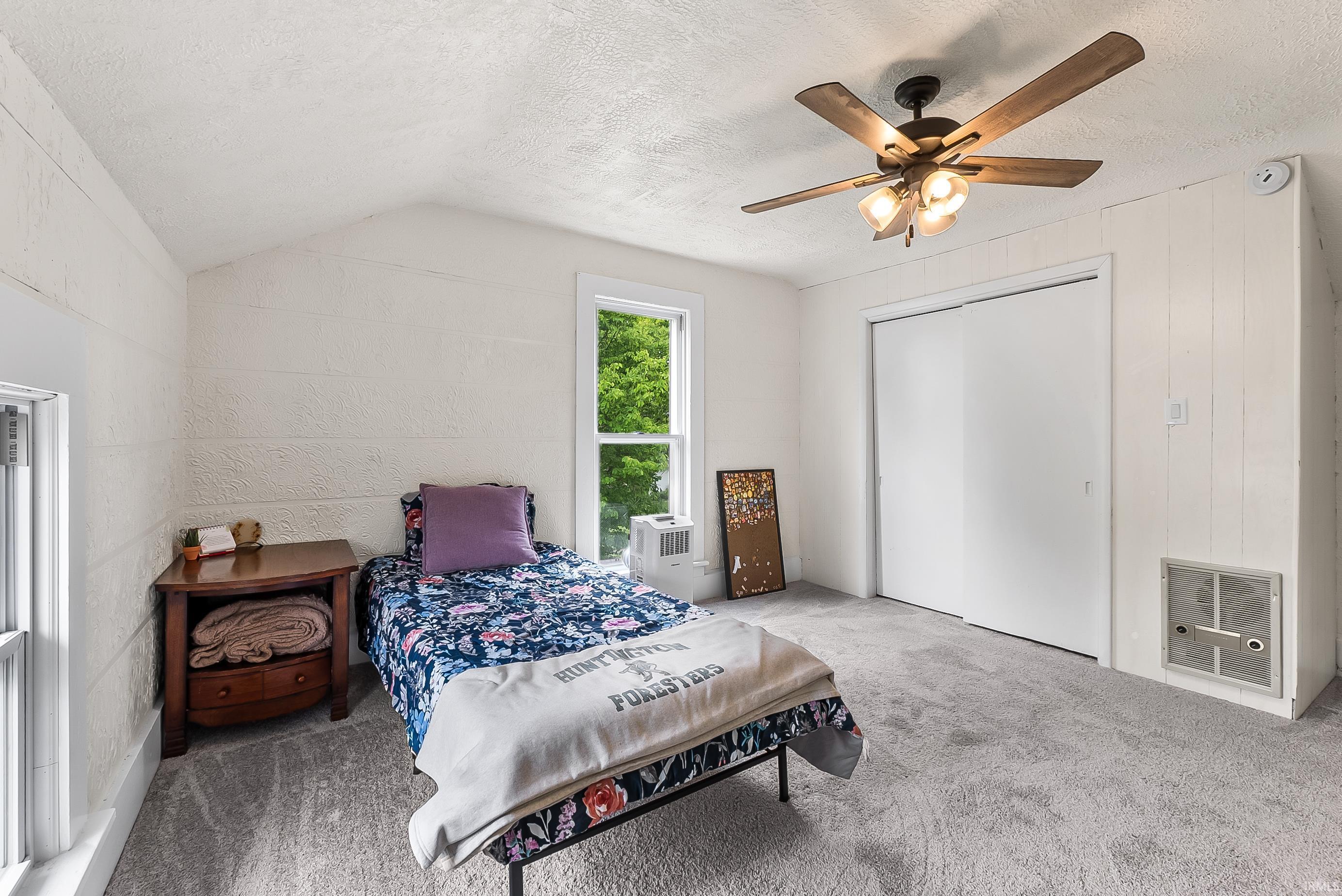 Interior room featuring white painted shiplap walls, light gray carpet flooring, and a ceiling fan with wood-finish blades