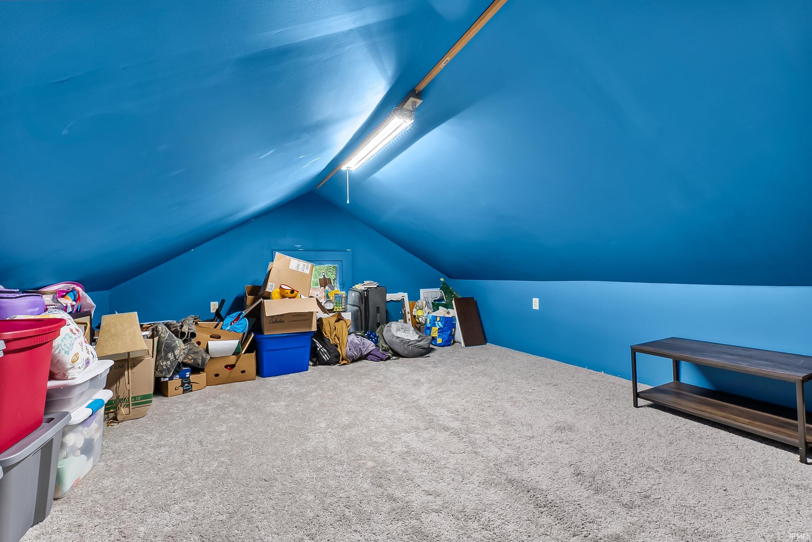 Attic space featuring sloped blue walls, light gray carpeting, and a built-in fluorescent light fixture