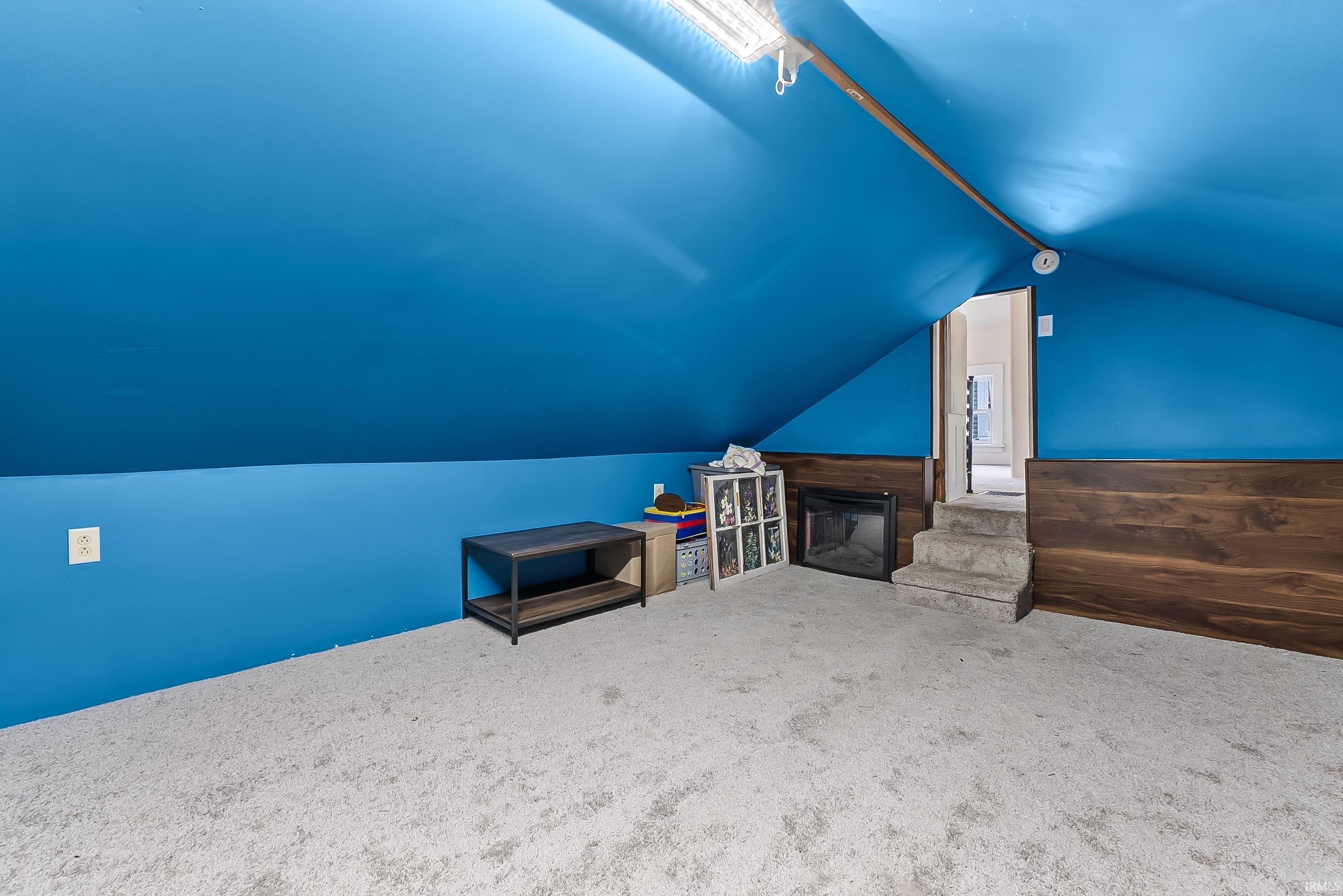 Carpeted attic space featuring sloped ceilings, a wood-paneled accent wall, a built-in fireplace unit, and a two-step entry