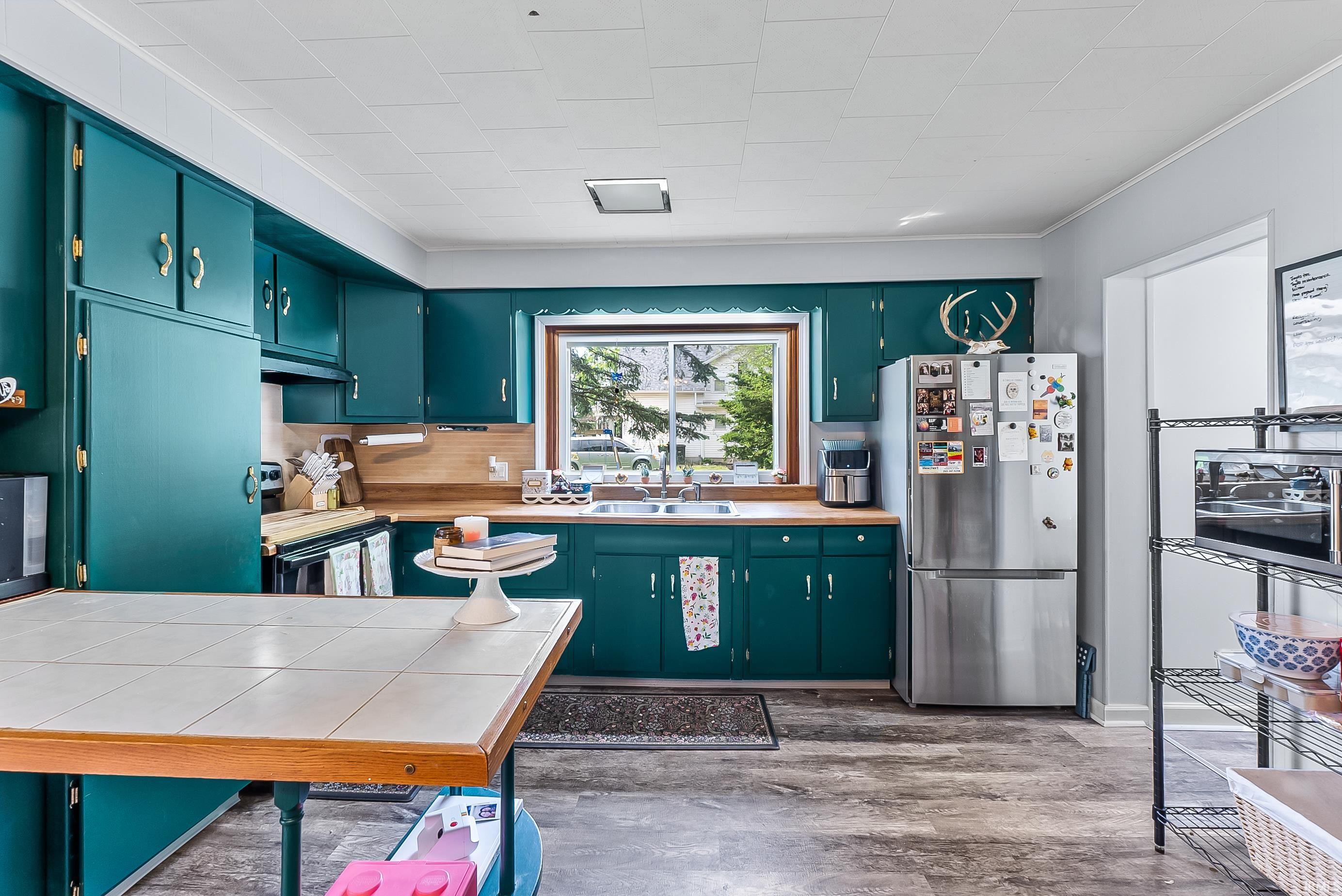 Kitchen featuring teal cabinetry, wood-finish countertops, and a stainless steel refrigerator