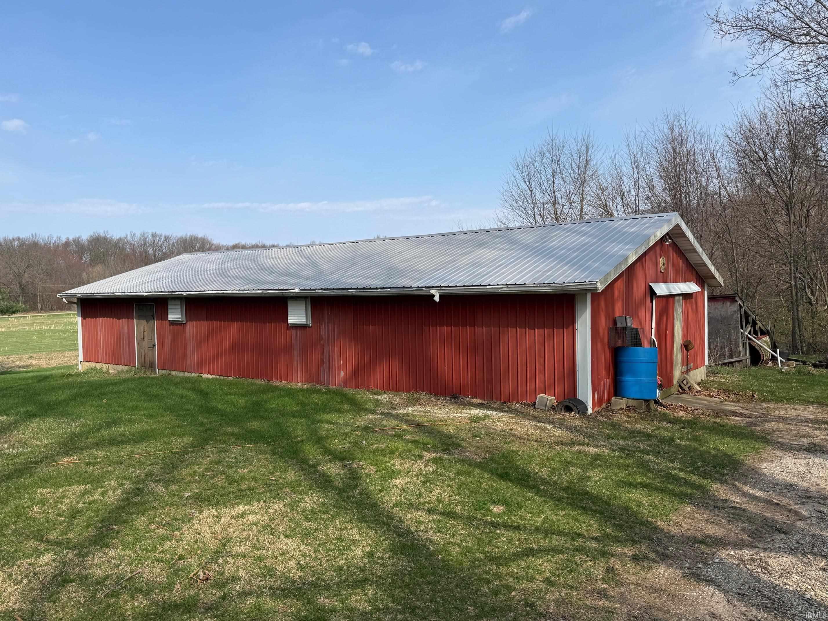 Red-sided outbuilding with a corrugated metal roof, multiple entry doors, and a partial gravel driveway