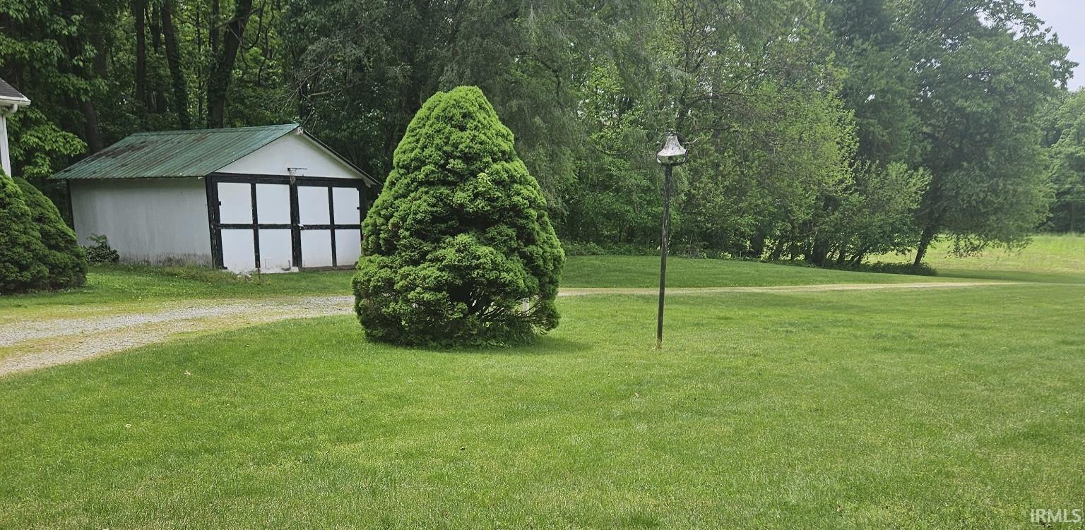Expansive green lawn with mature trees, a gravel driveway, and a detached outbuilding featuring a green roof and white and black garage doors