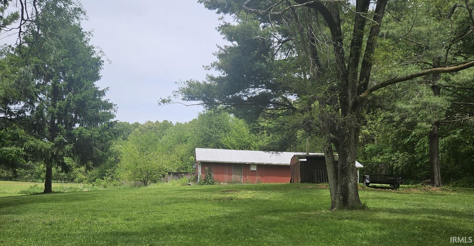 Expansive green lawn with mature trees and a red barn featuring an attached carport
