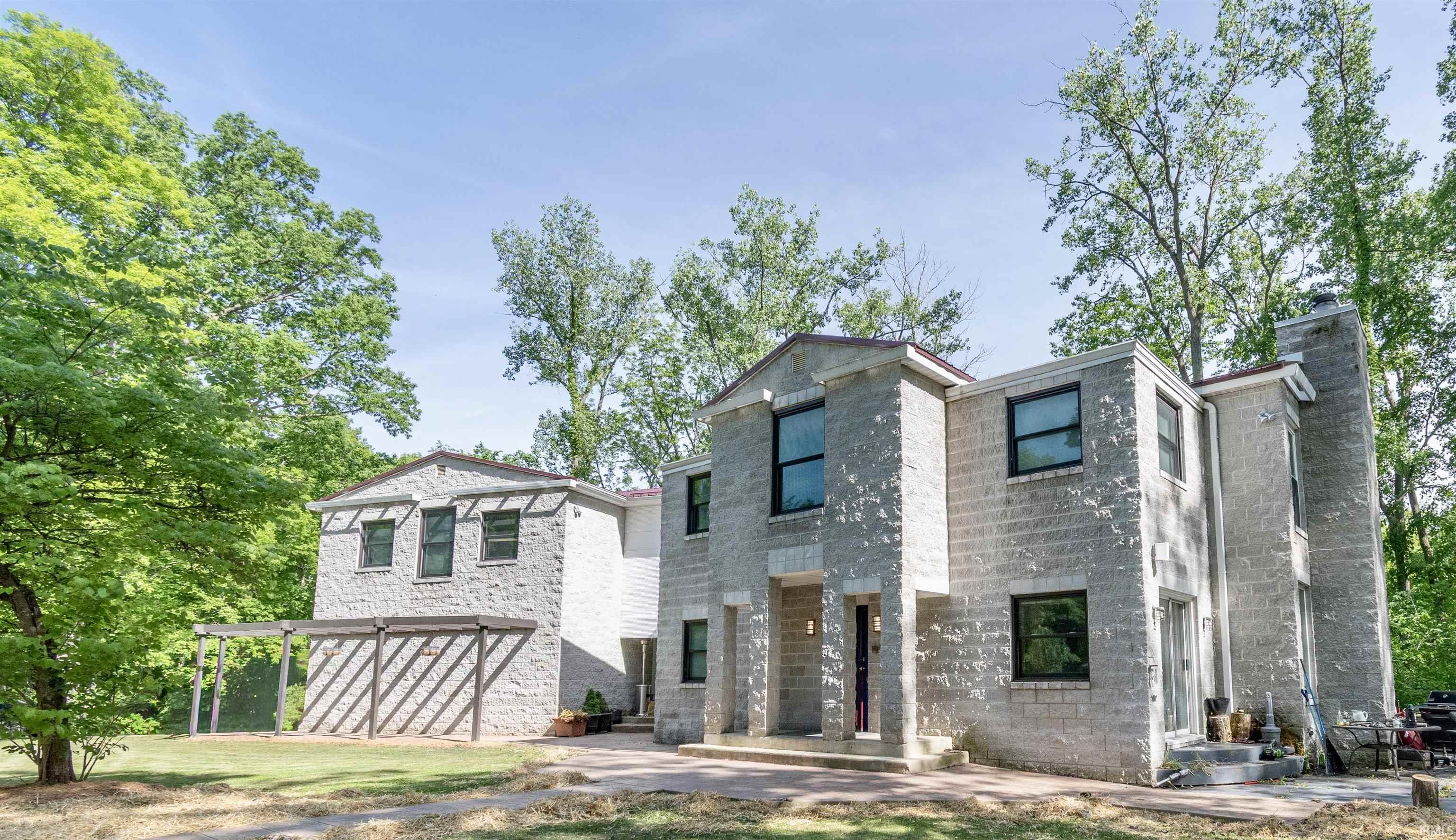 Two-story block construction residence featuring a prominent chimney, multiple windows with dark framing, and a pergola structure