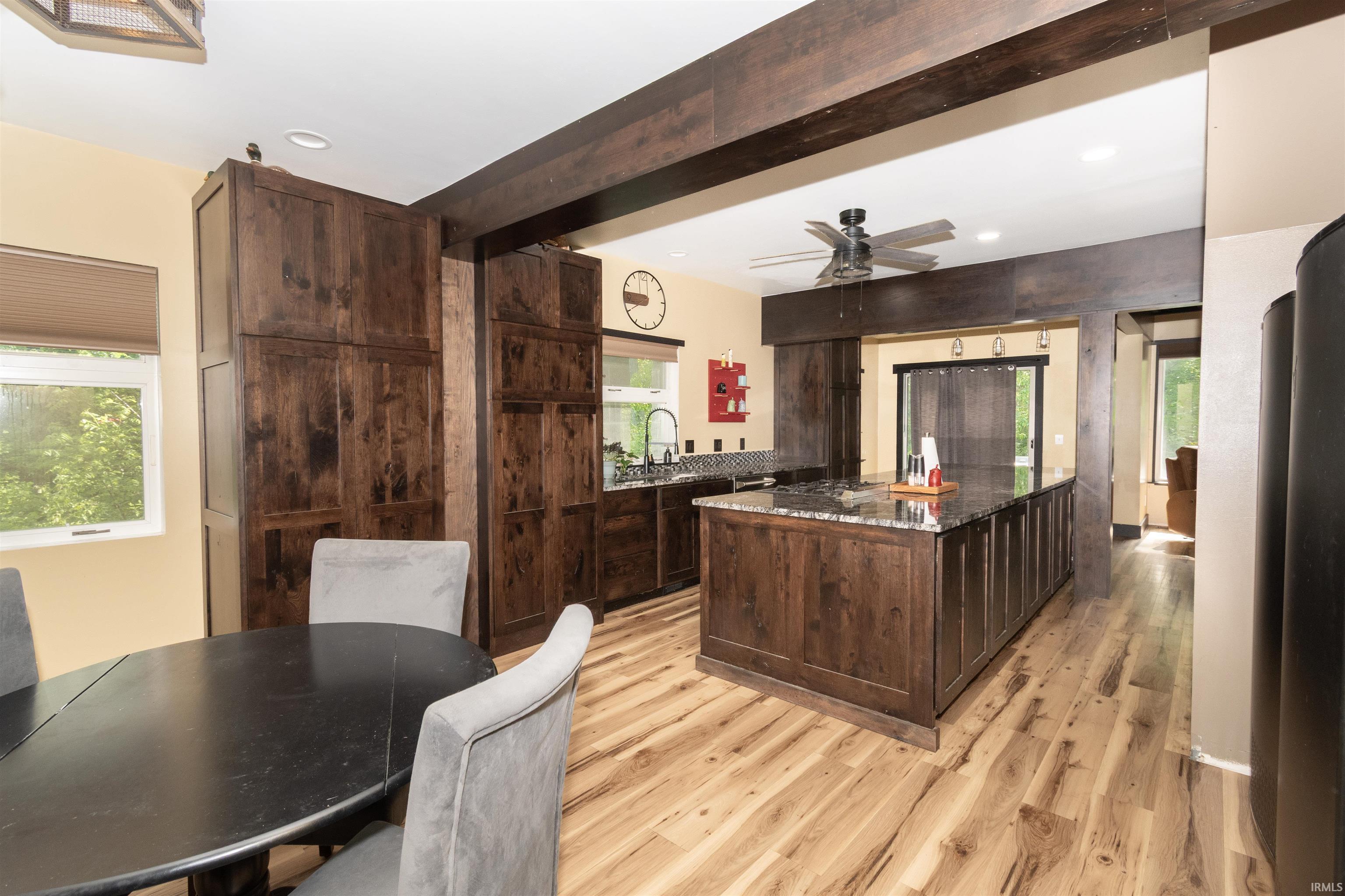 Kitchen featuring a dark wood-finish island with a stone countertop, coordinating wood-finish cabinetry, wood-finish flooring, and exposed ceiling beams
