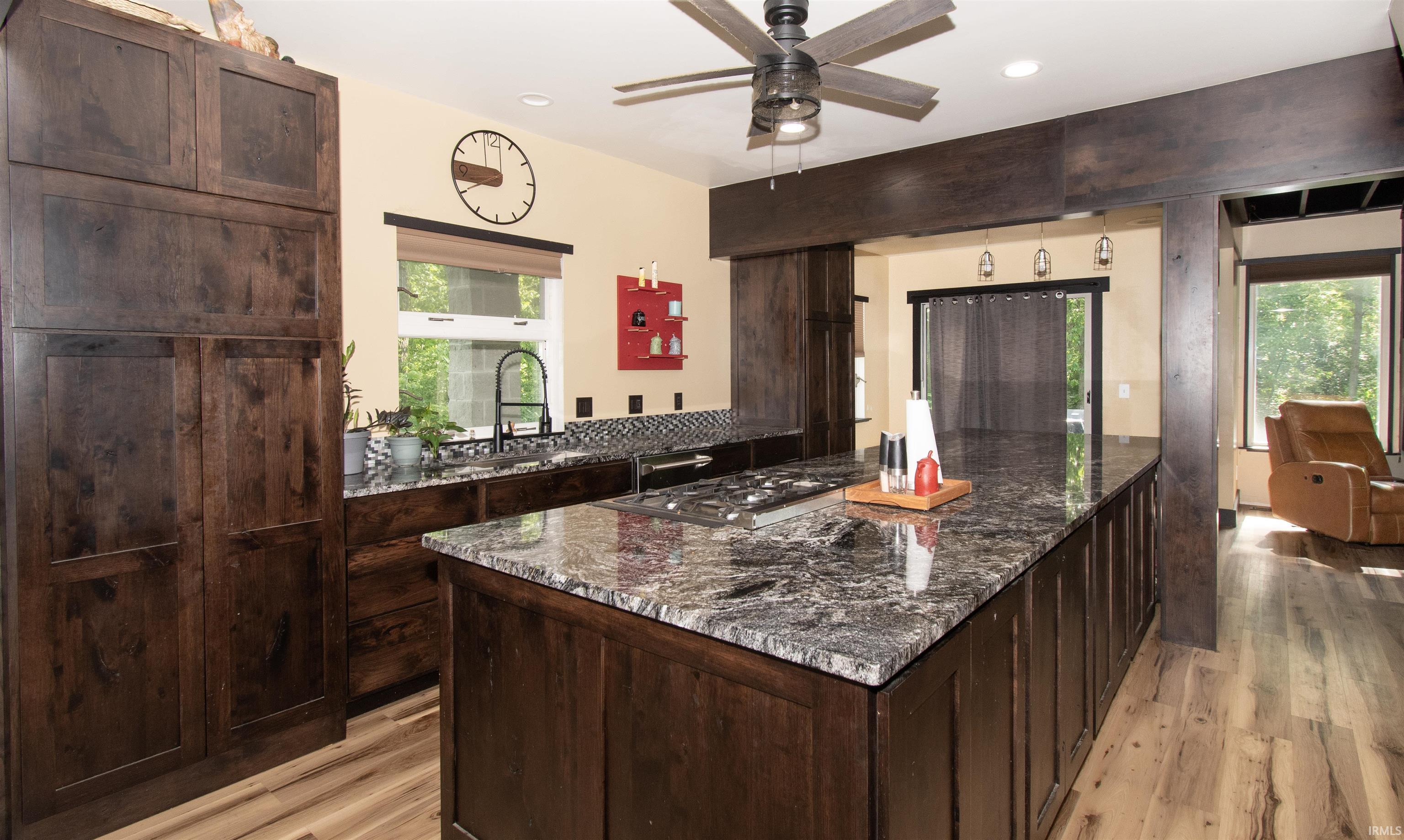 Gourmet kitchen featuring a large island with a cooktop, dark wood cabinetry, granite countertops, and wood-finish flooring