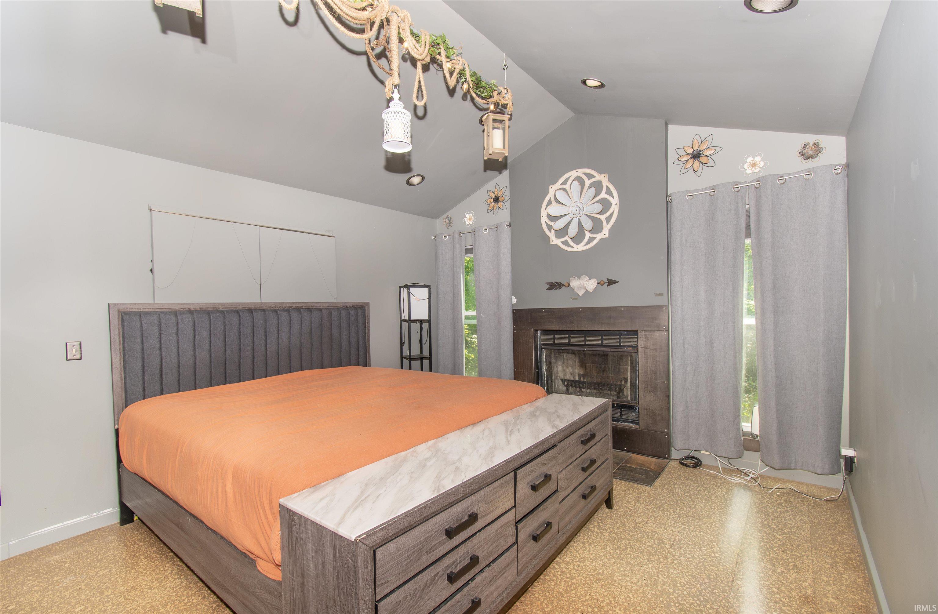 Vaulted ceiling bedroom featuring a dark wood-finish fireplace, recessed lighting, and light-toned flooring