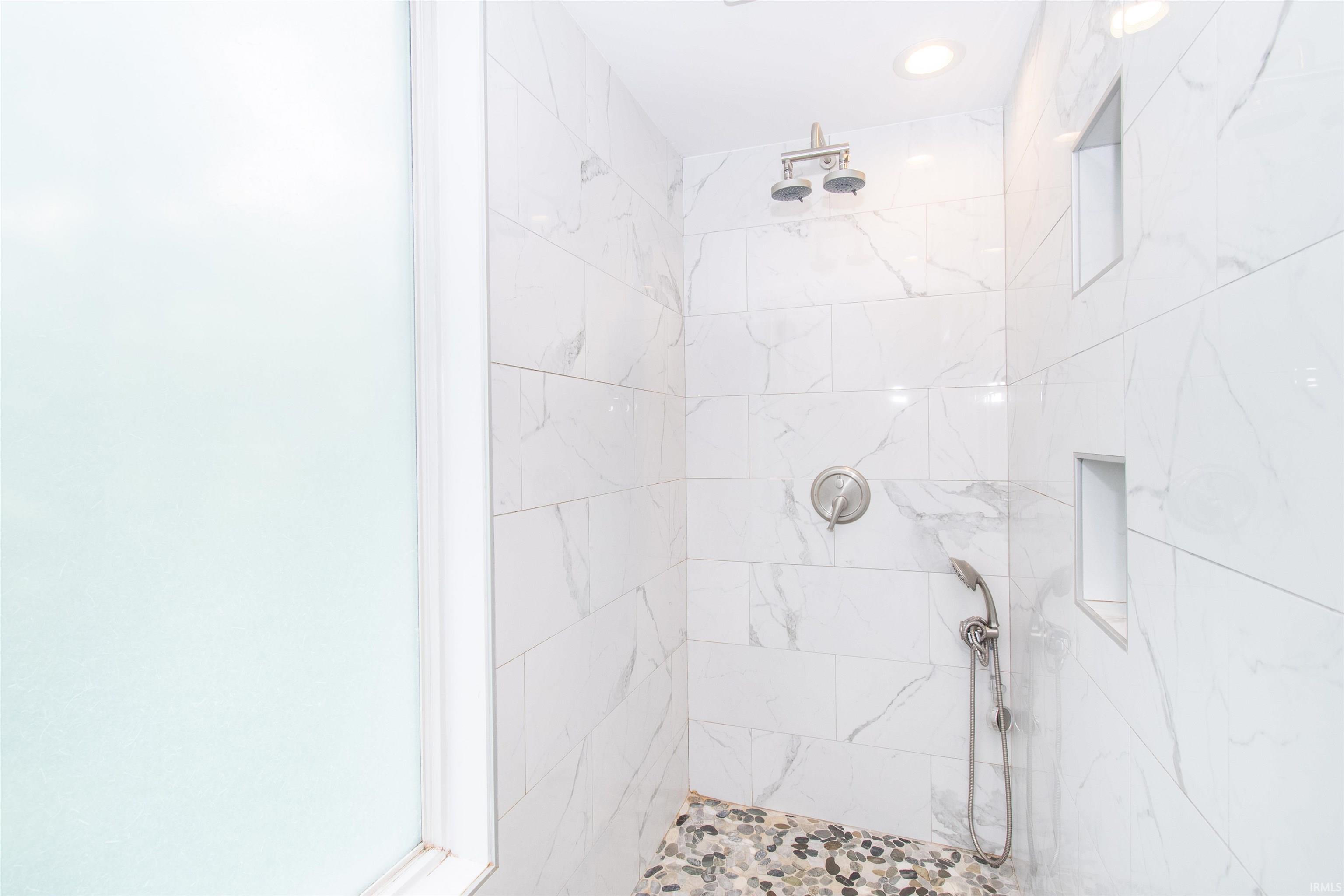Shower enclosure featuring large format white marble-look tile walls and a pebble-stone floor