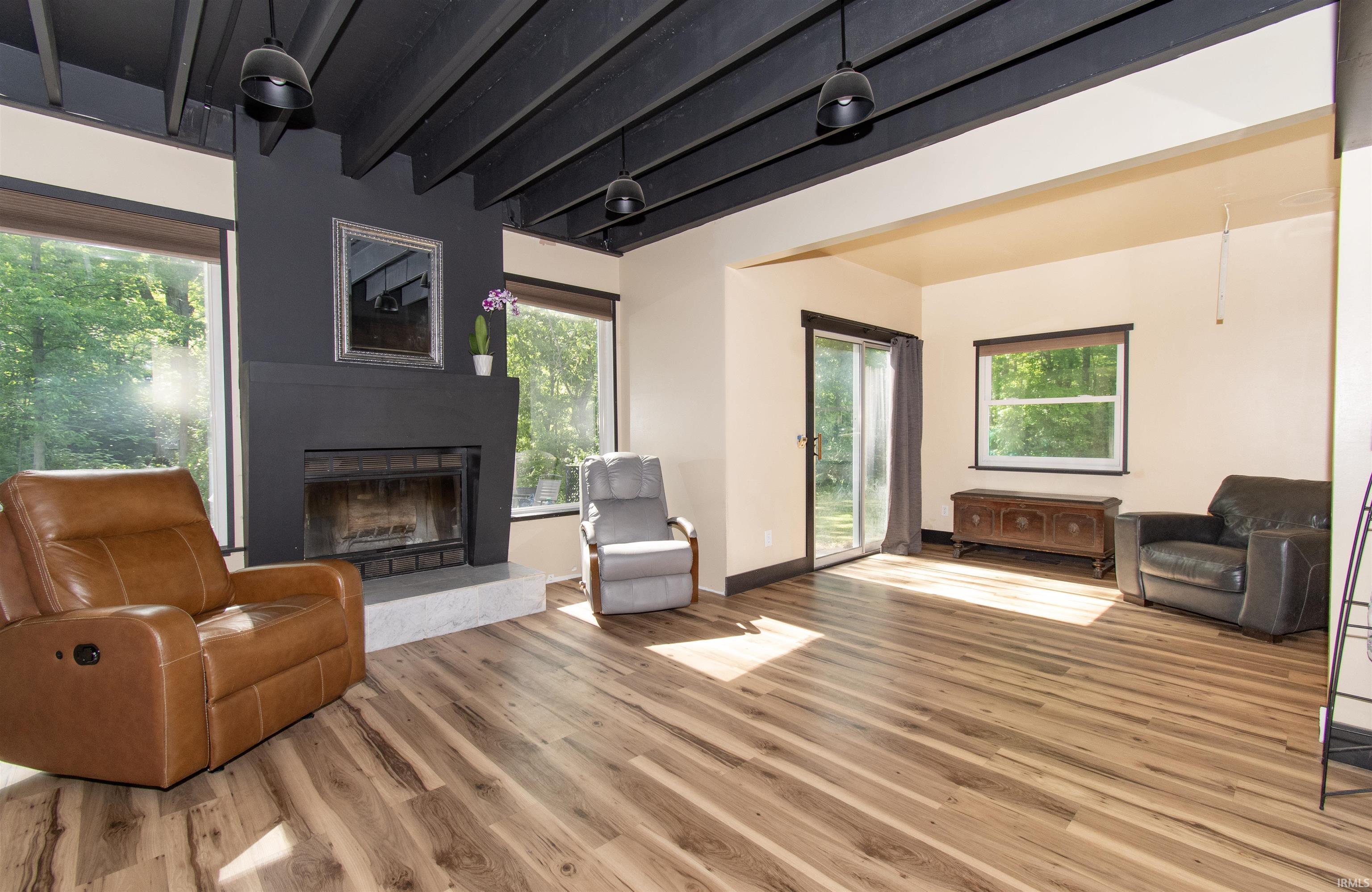 Living space featuring wood-finish flooring, a contemporary fireplace with a contrasting mantel, exposed black ceiling beams, and large picture windows