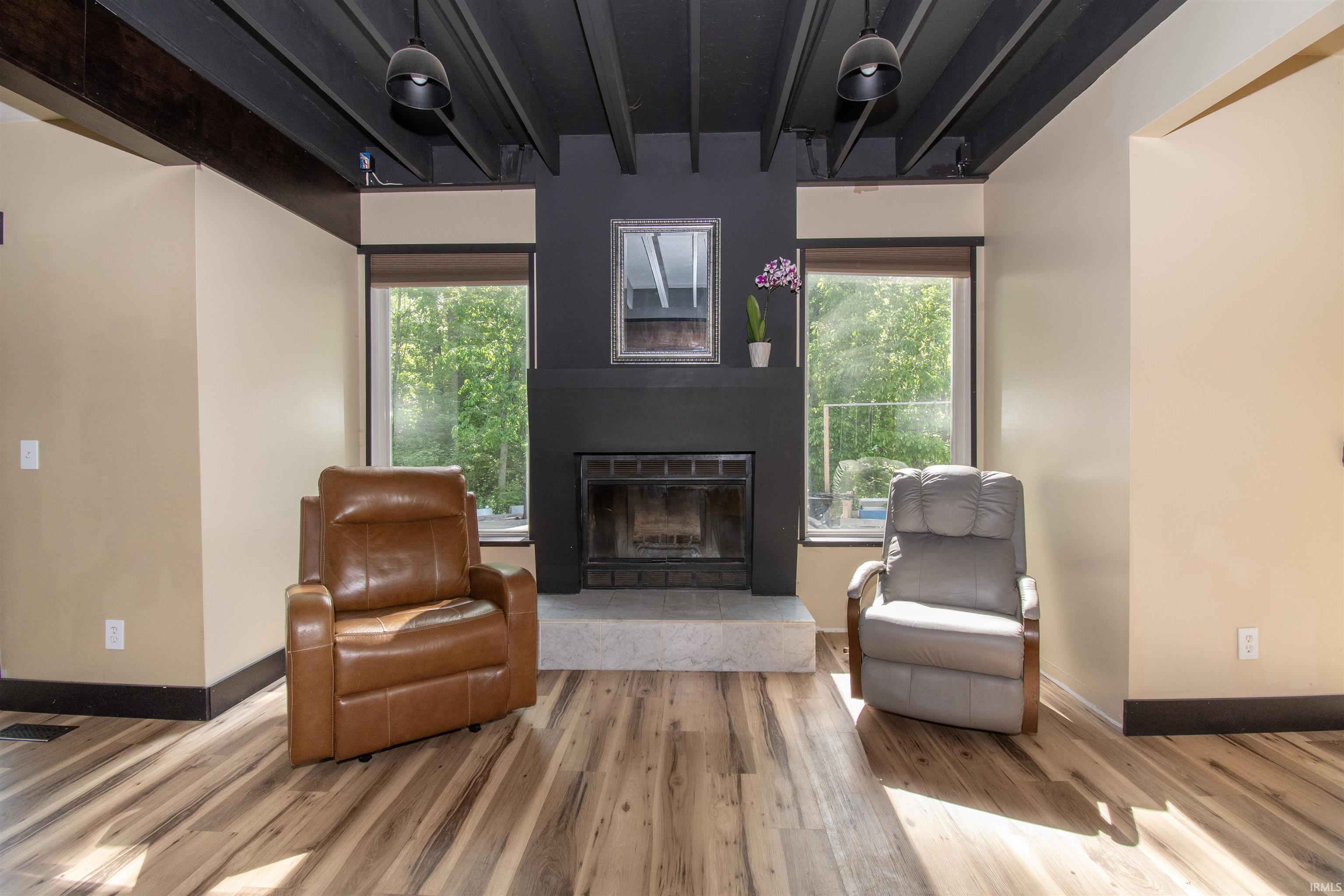Living area featuring wood-finish flooring, a black fireplace with a light-toned hearth, and two large windows