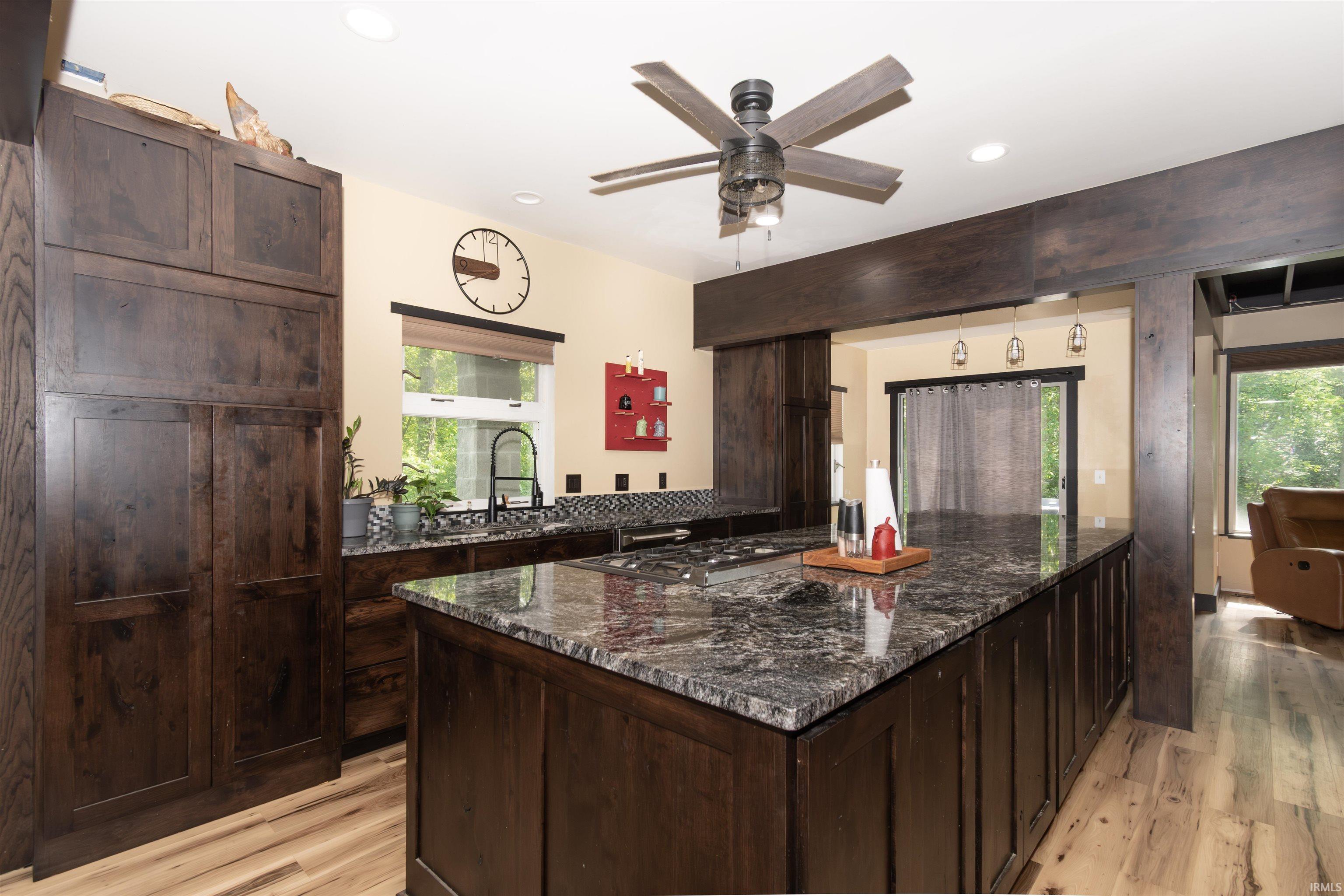 Kitchen featuring an expansive island with a gas cooktop, dark wood-finish cabinetry, speckled stone countertops, and wood-finish flooring