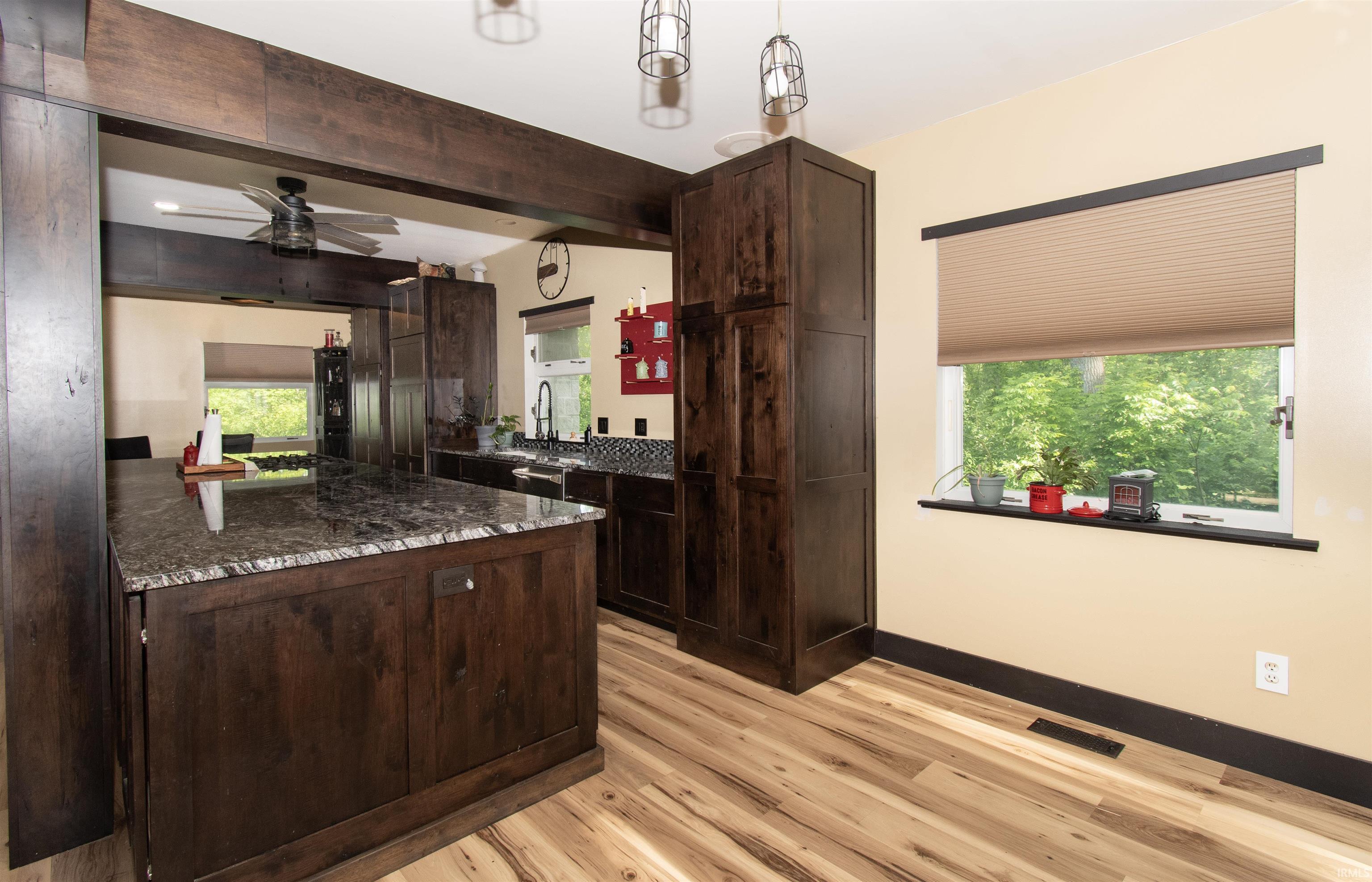Kitchen featuring wood-finish flooring, dark wood cabinetry, and a central island with a stone-finish countertop