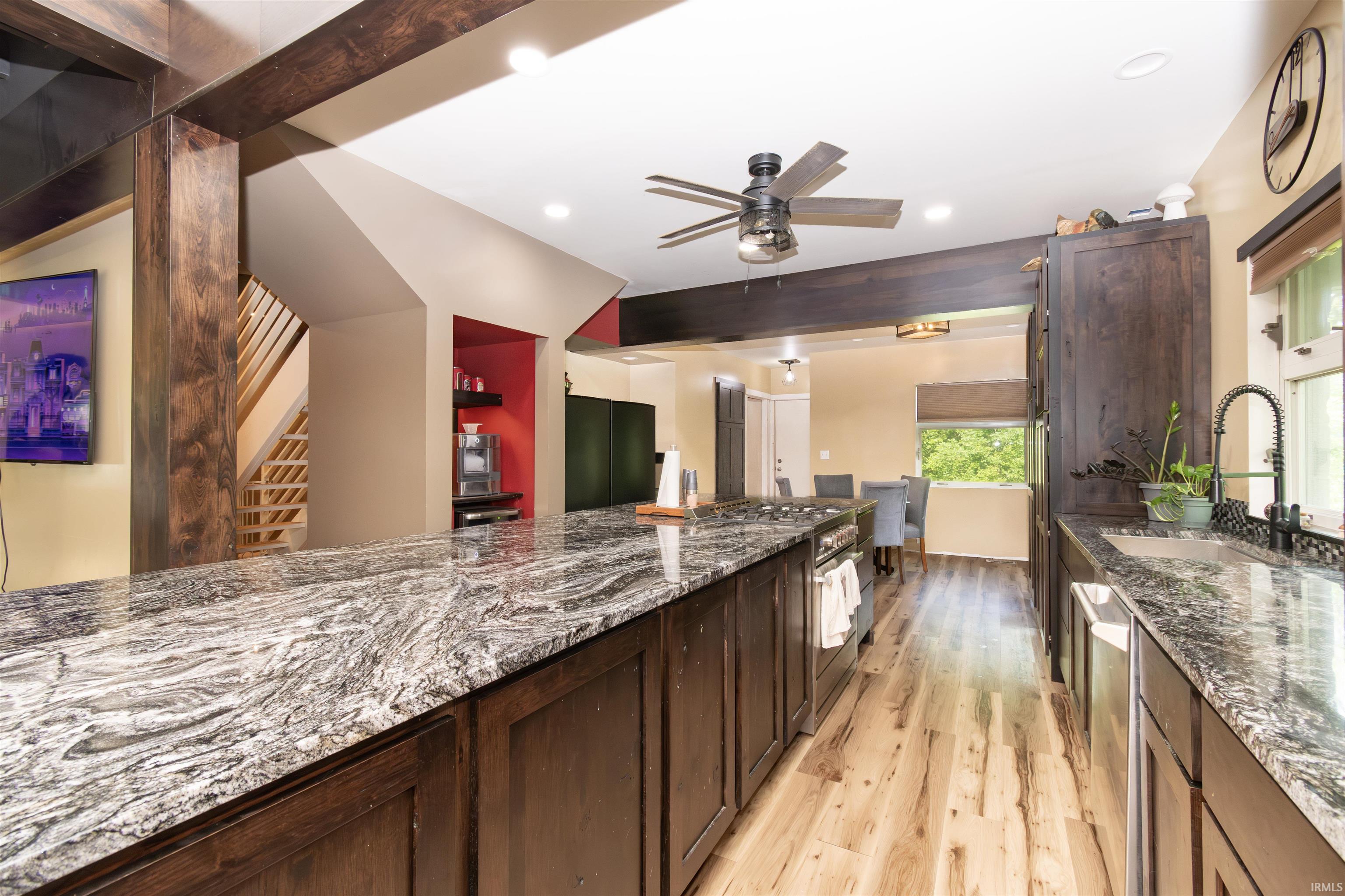 Kitchen featuring expansive counter space, wood-finish flooring, dark wood cabinetry, a stainless steel dishwasher, and a ceiling fan