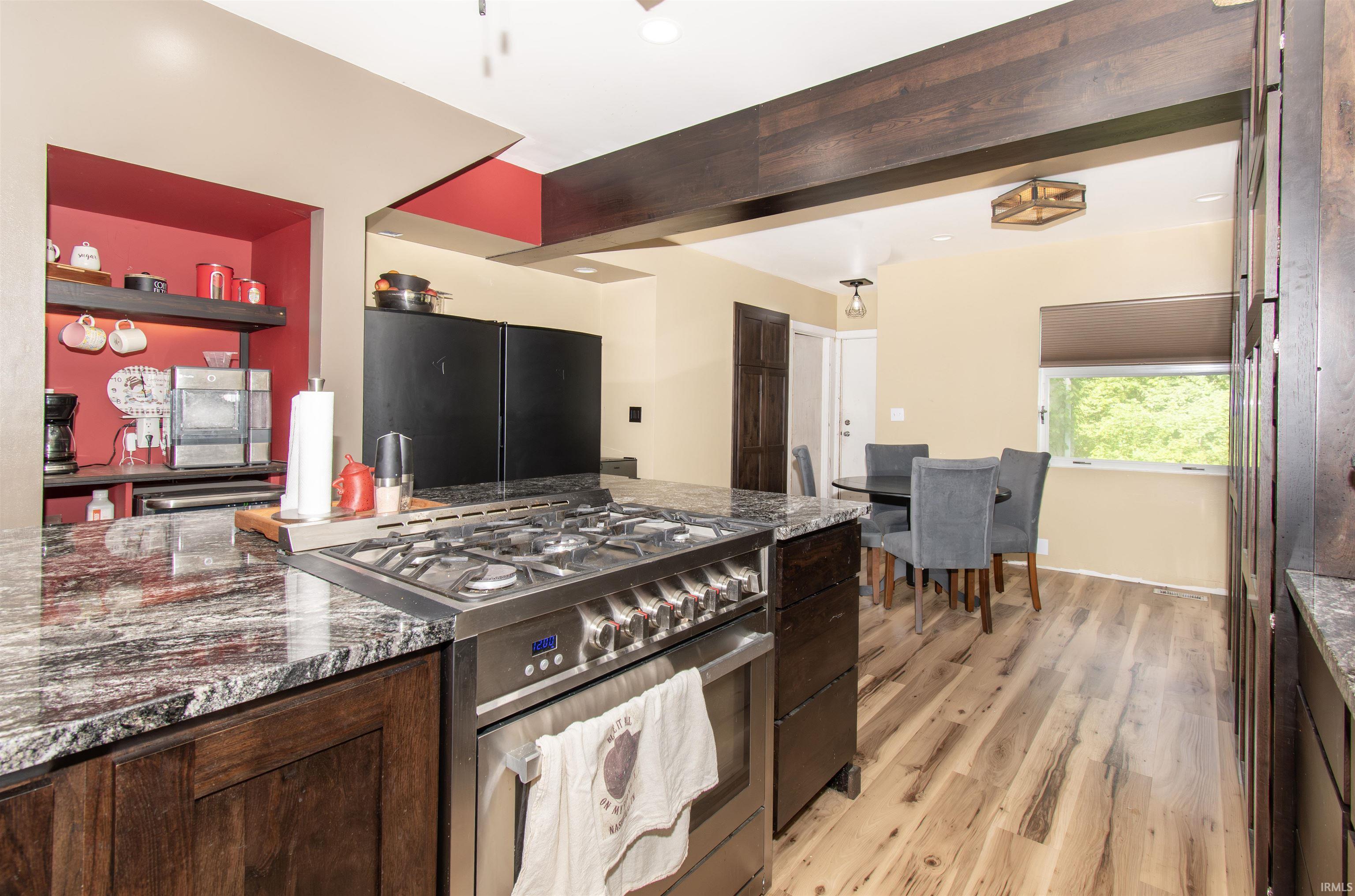 Gourmet kitchen with a stainless steel gas range, granite countertops, wood-finish flooring, and dark wood cabinetry