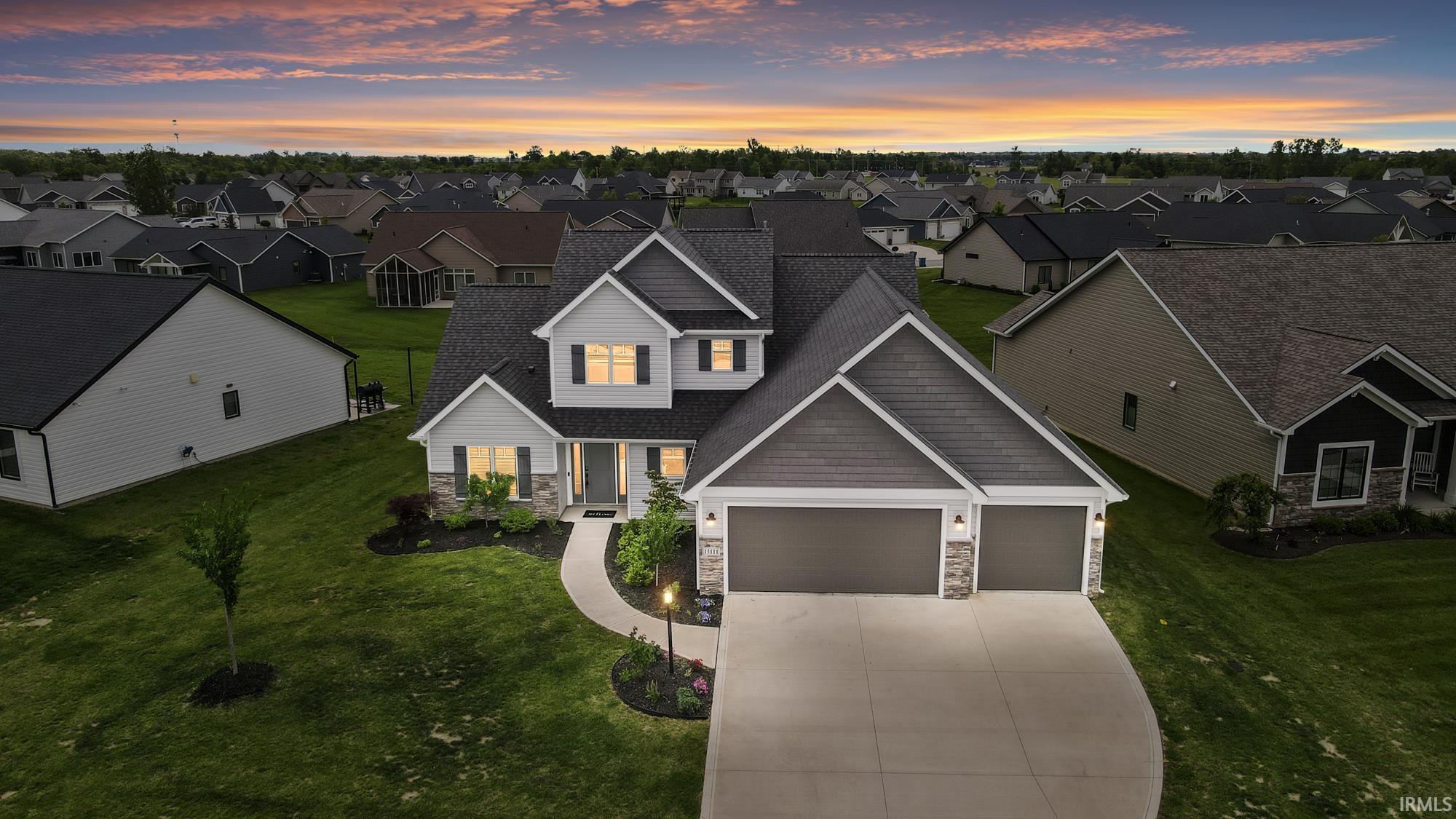 Contemporary home exterior featuring a multi-gabled roofline, stone and siding facade, two-car garage, and an illuminated entryway