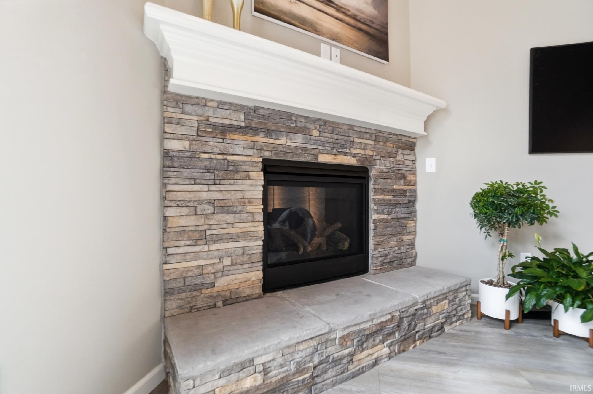 Stone-faced fireplace with a gas insert, substantial white mantel, and integrated stone hearth seating