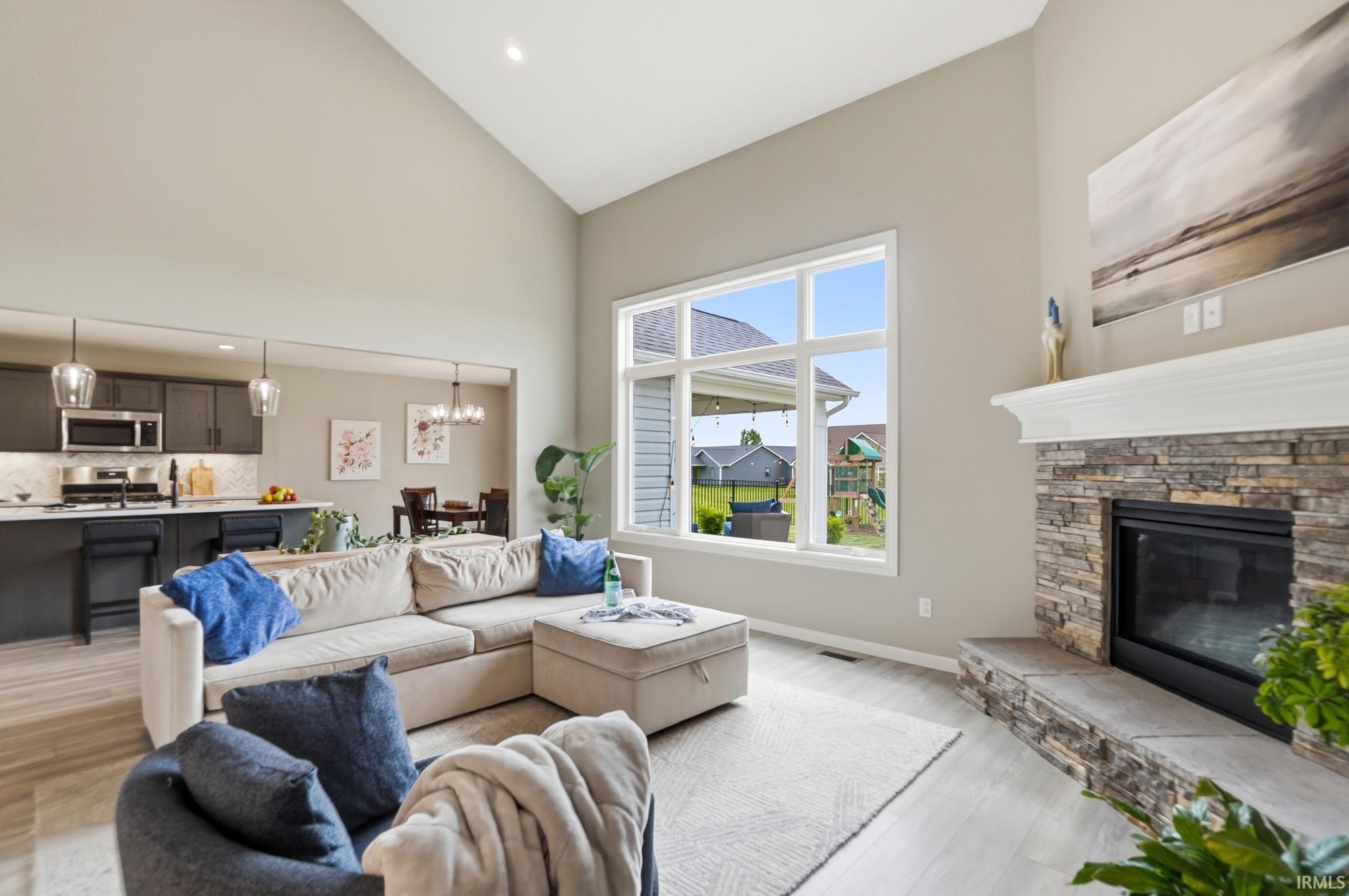 Vaulted ceiling living room featuring a stone-clad fireplace with a mantle, large picture windows, wood-finish flooring, and recessed lighting