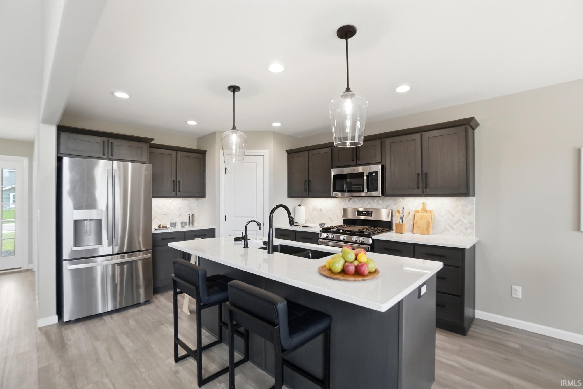 Kitchen featuring dark wood-finish cabinetry, stainless steel appliances, a white herringbone backsplash, and wood-finish flooring
