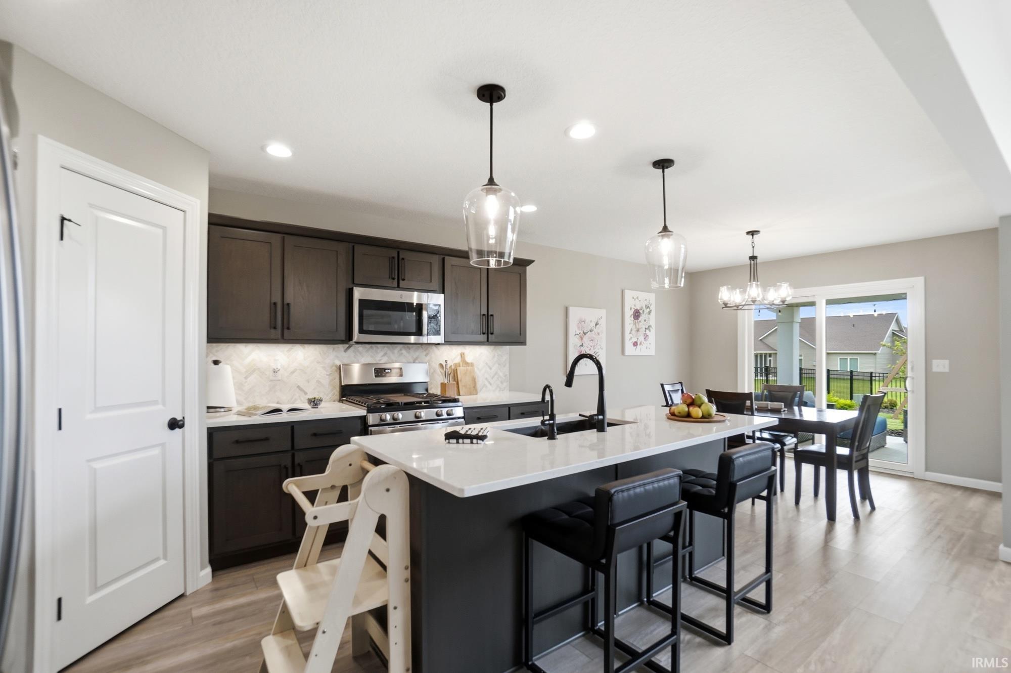 Contemporary kitchen featuring dark wood cabinetry, stainless steel appliances, a white stone countertop island with seating, and a decorative tile backsplash