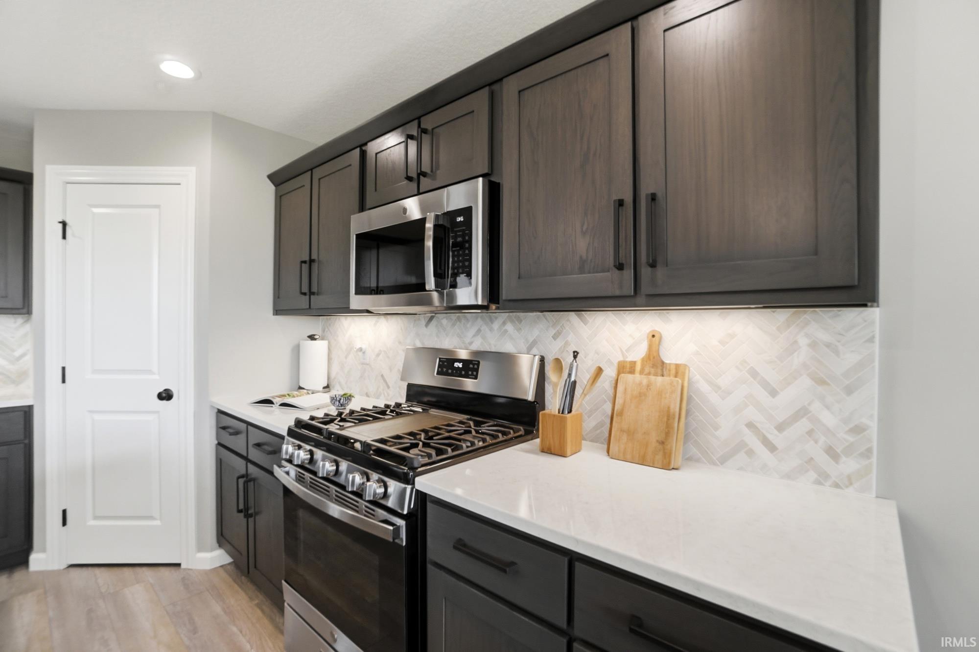 Kitchen featuring dark wood-finish cabinetry, white countertops, a stainless steel gas range, and a stainless steel microwave