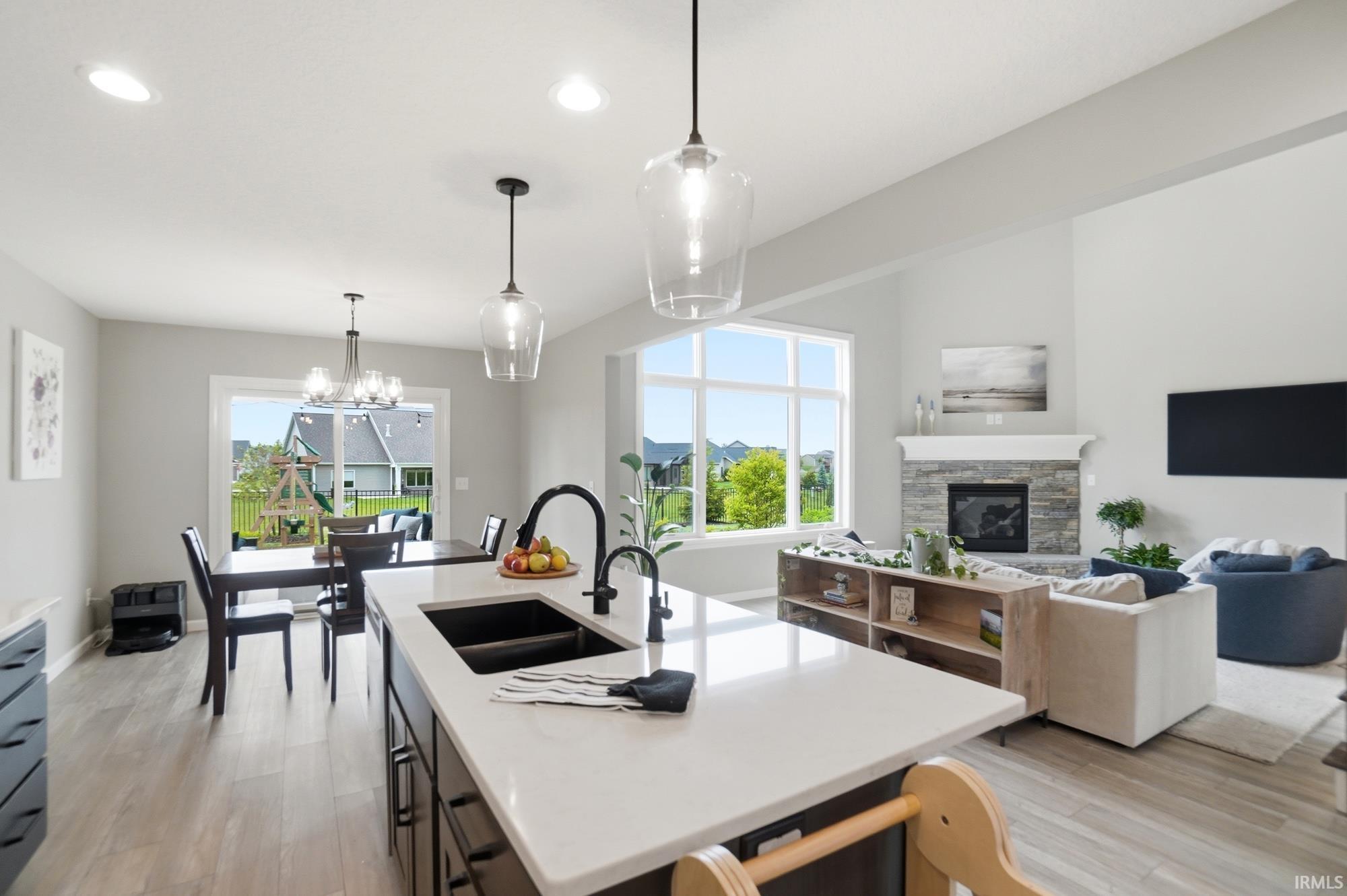 Spacious open-concept living area featuring a kitchen island with a black farmhouse sink, a dining area with a contemporary chandelier, and a living room with a stone fireplace