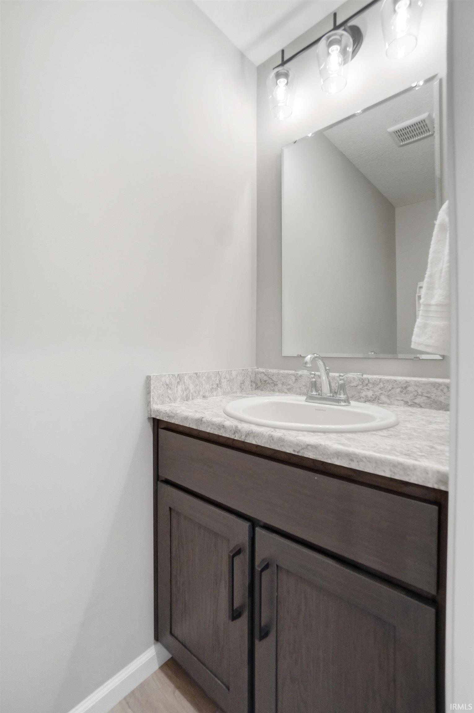 Bathroom vanity featuring a light-colored countertop, integrated sink, and dark wood-finish cabinetry with modern black hardware
