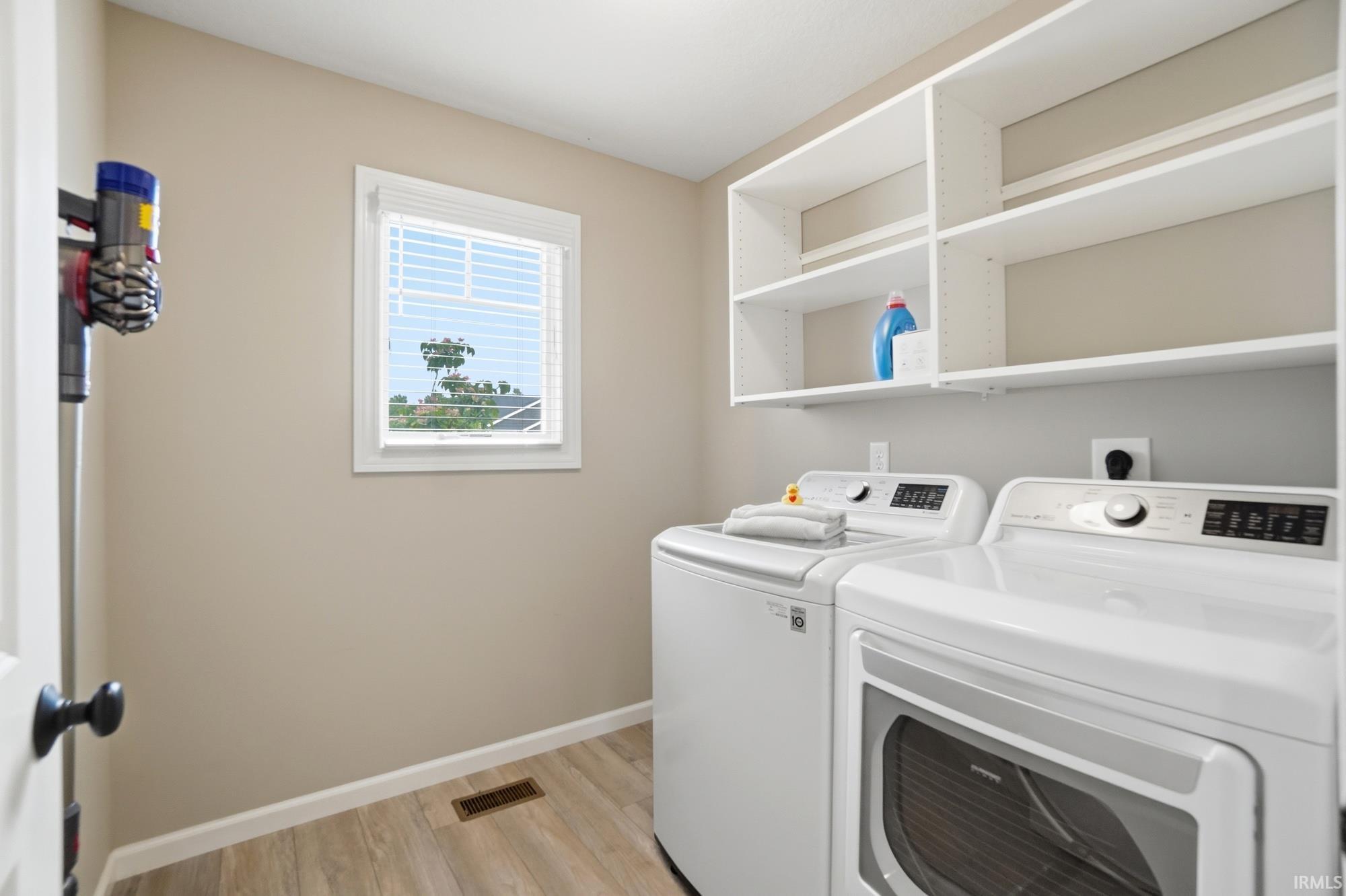 Dedicated laundry area featuring wood-finish flooring, a window with blinds, and built-in white shelving